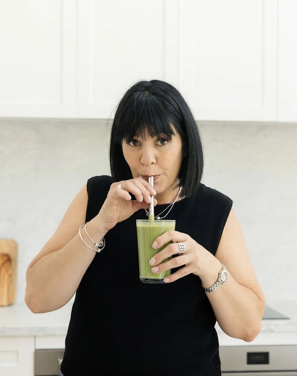 Susie the founder of Turnip Nutrition, with black hair drinking a green smoothie from a glass with a straw in a modern kitchen.
