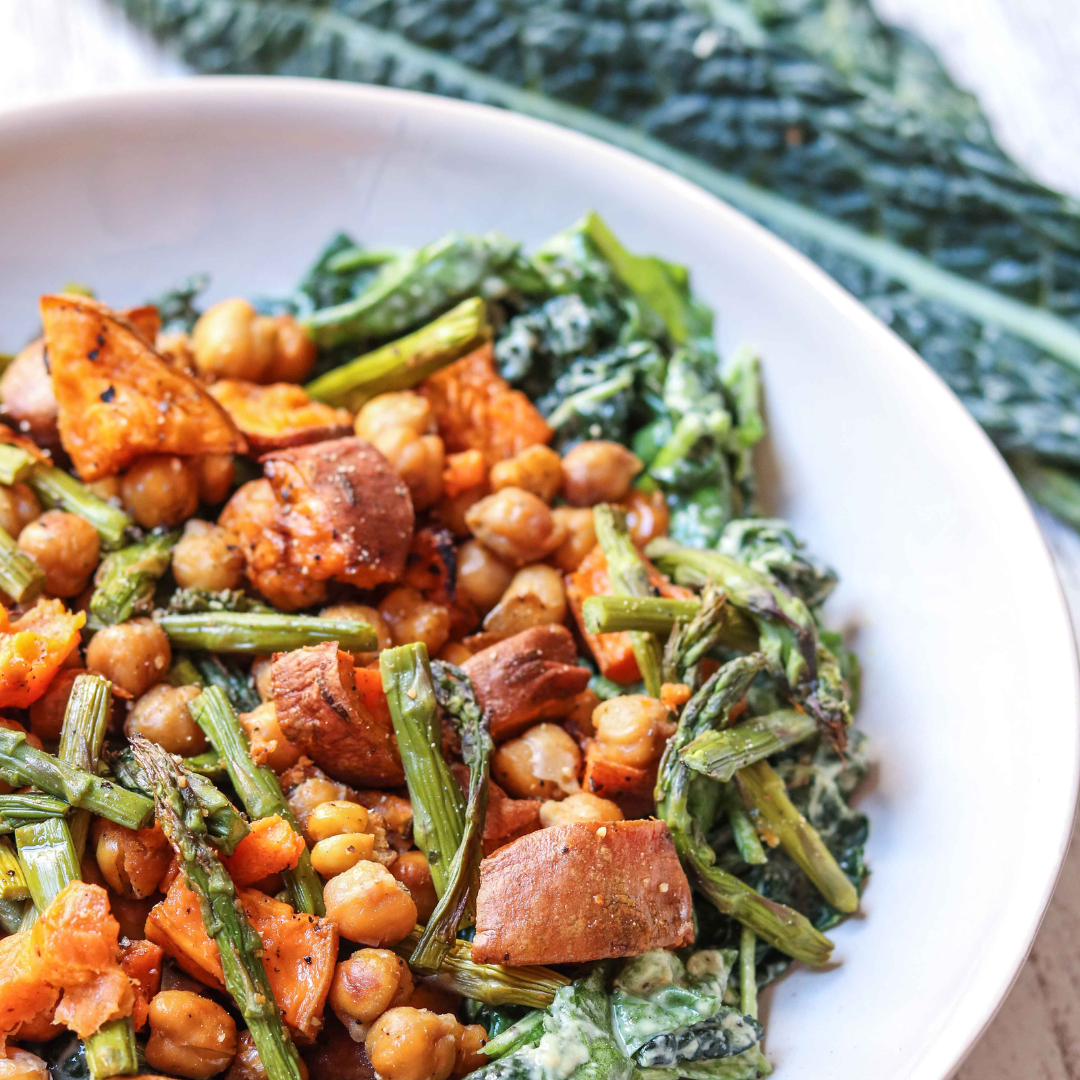 Close-up of a white bowl filled with roasted chickpeas, chopped sweet potatoes, and greens, possibly kale or spinach.