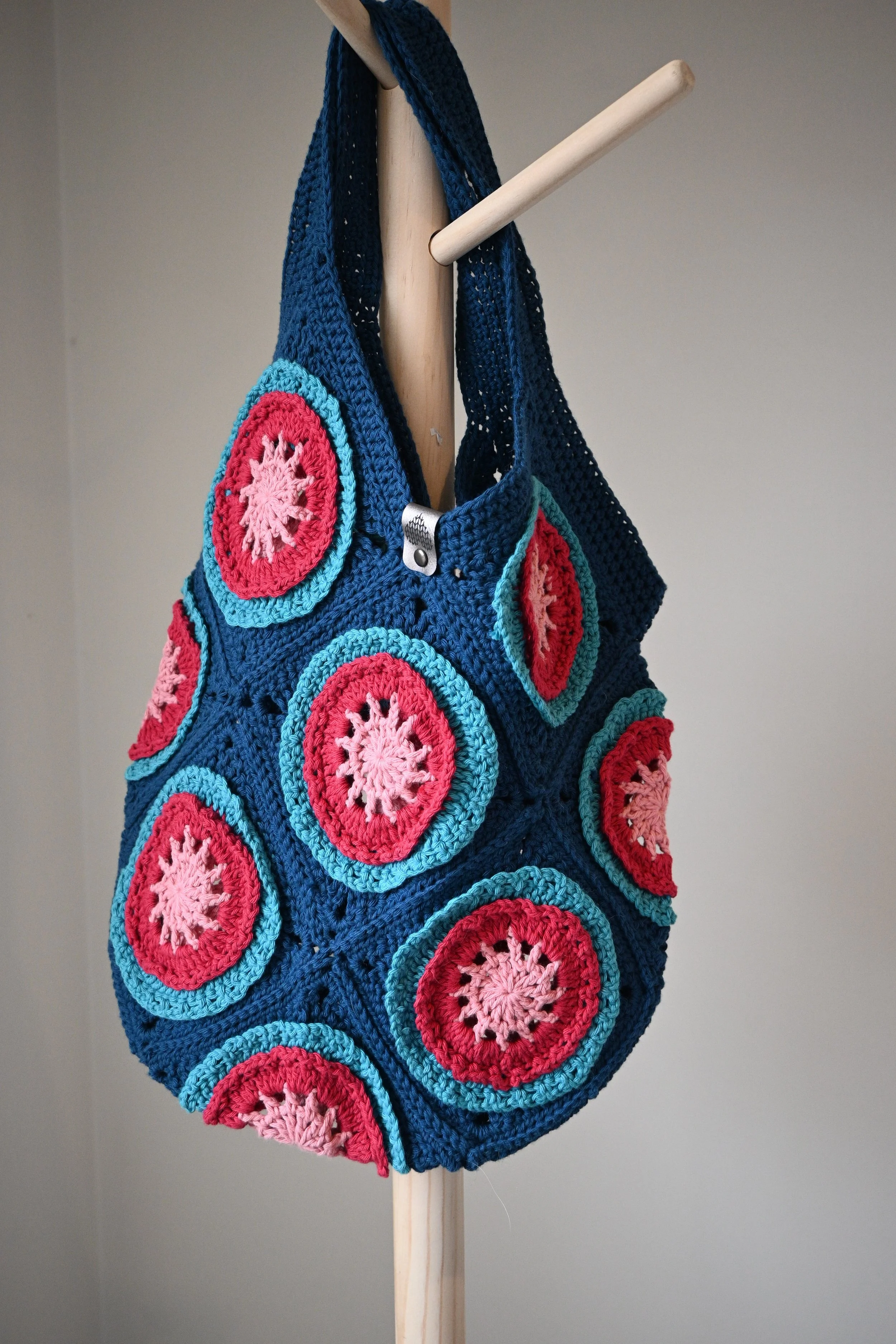 Crocheted bag with colorful circular patterns hanging on a wooden stand.