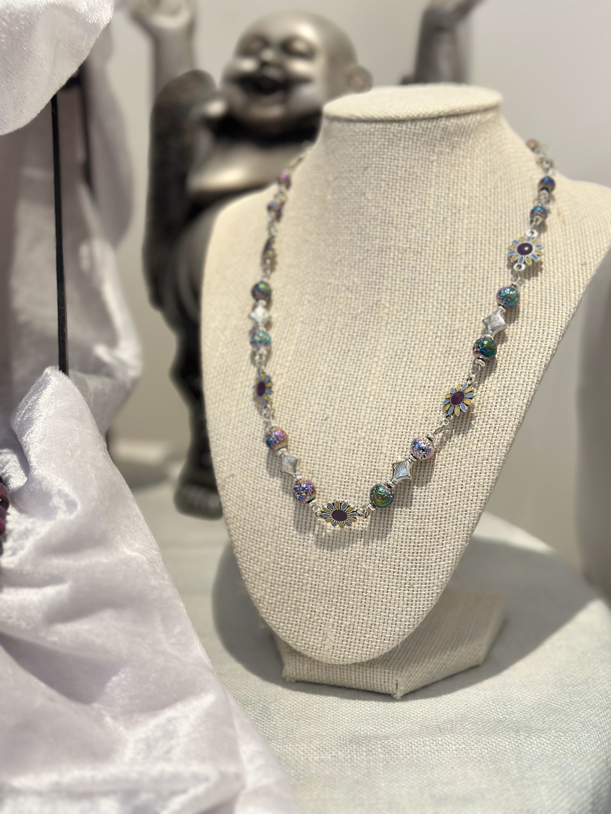 Jewelry display with colorful beaded necklace and a smiling statue in the background.