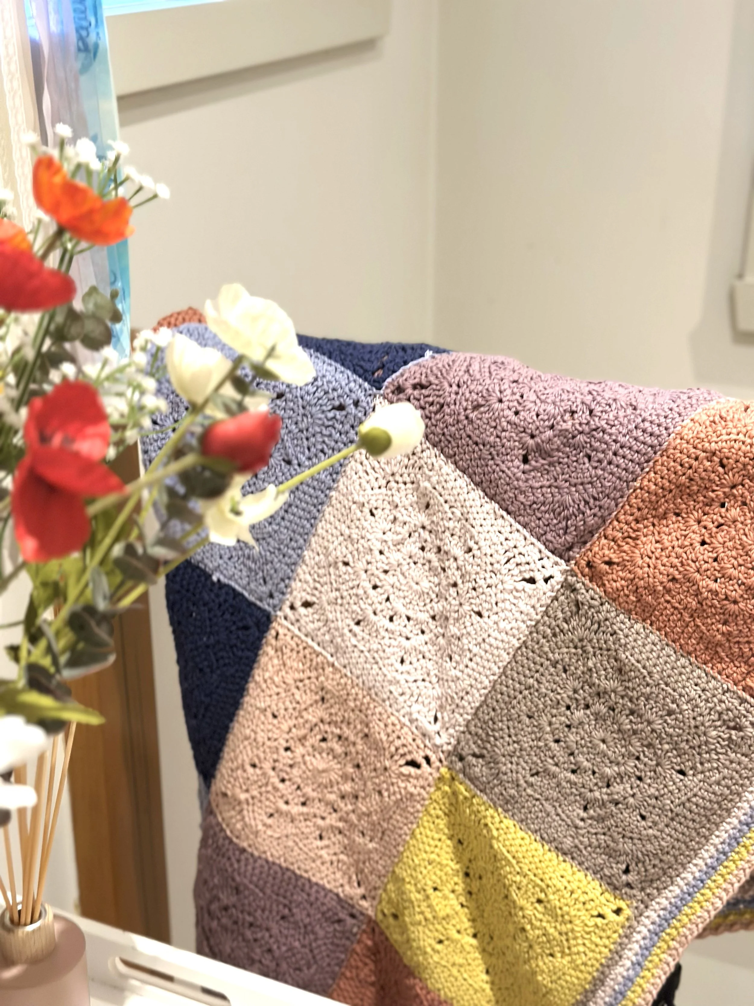 Colorful crocheted blanket on a chair with flowers in the foreground