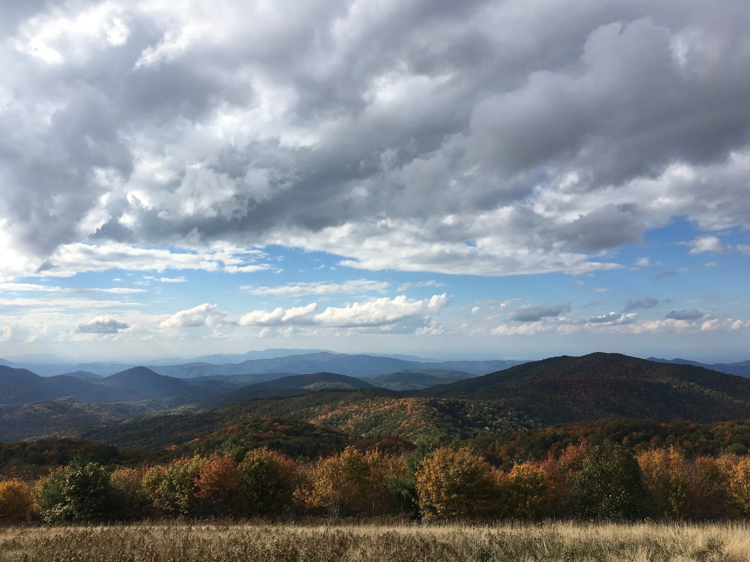 Scenic view of mountainous landscape with rolling hills covered in autumn-colored trees and a cloudy sky overhead.