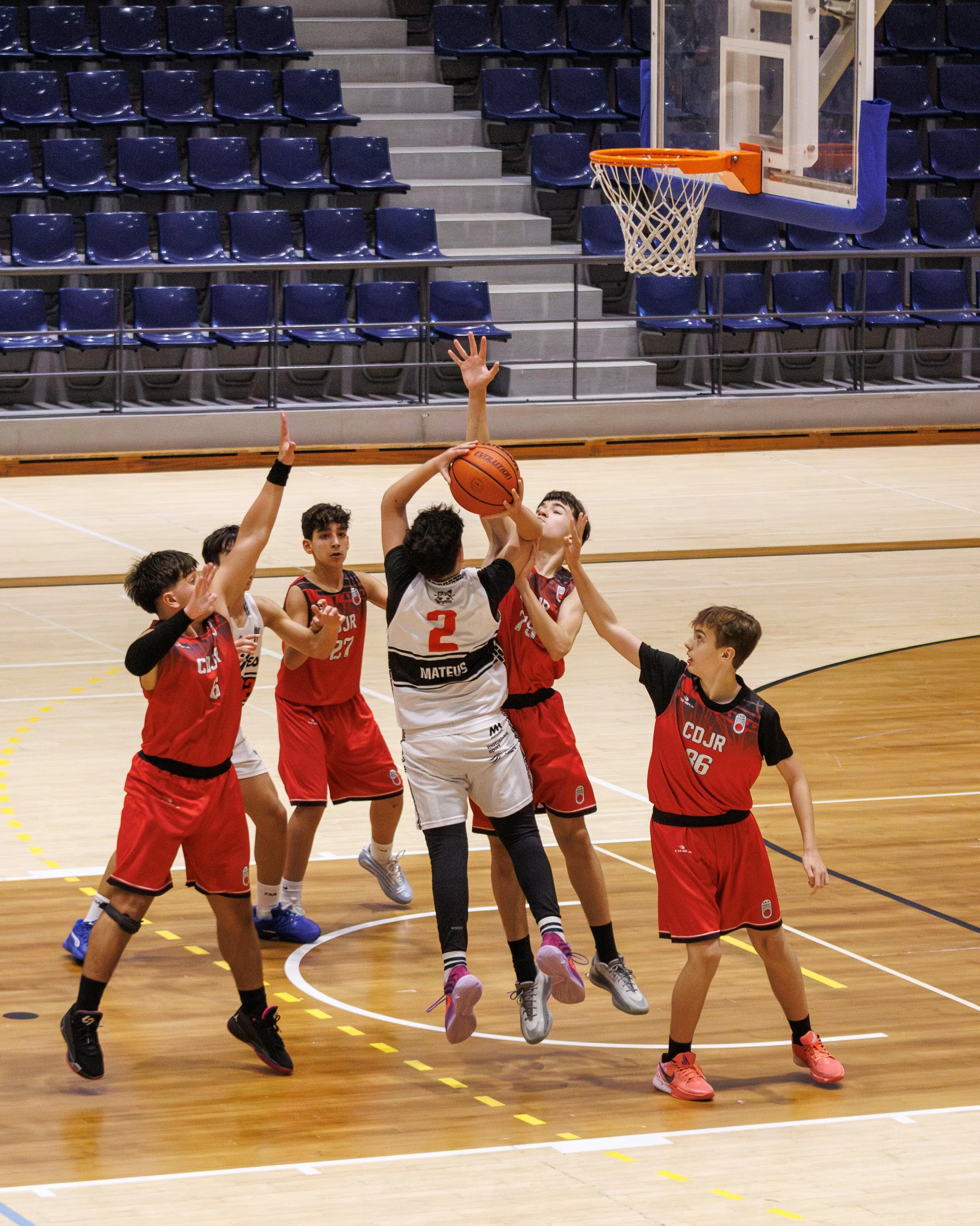 Young boys playing basketball in a gym, with one attempting a shot while several others try to block or defend.