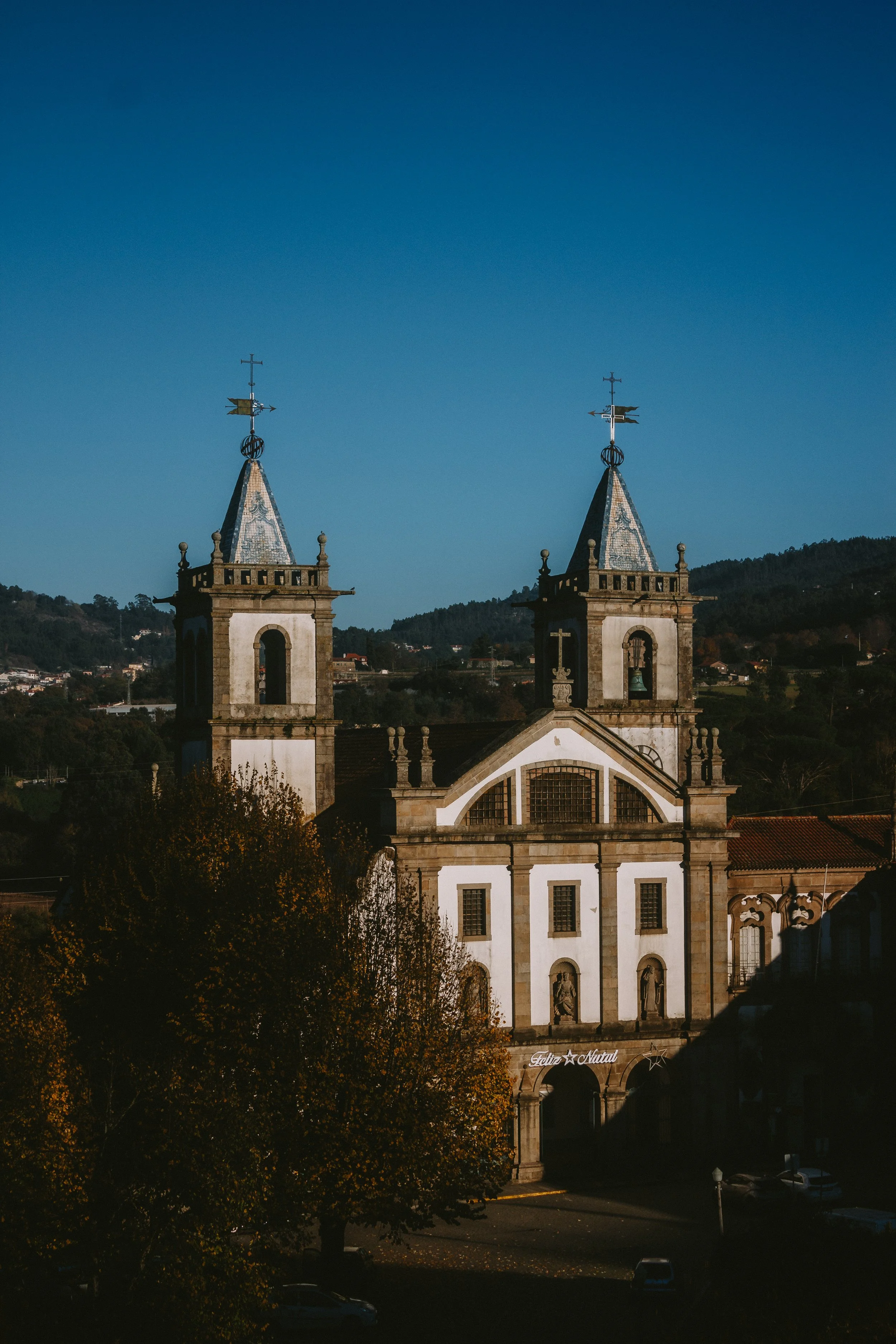 A historic church with two steeples topped with weather vanes, set against a mountainous landscape and a clear blue sky.