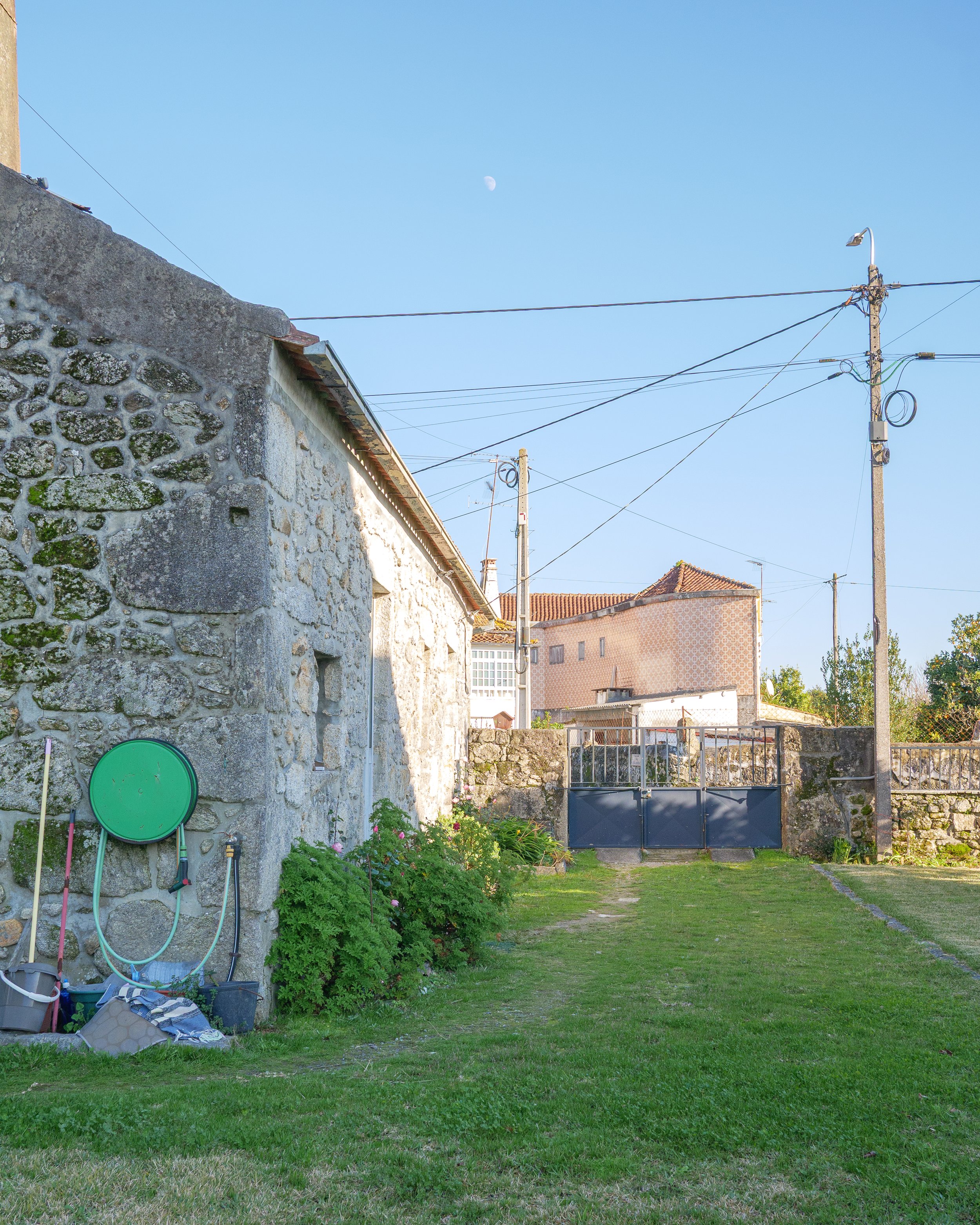 Backyard scene with stone house, garden, and utility poles under a clear sky with visible moon.