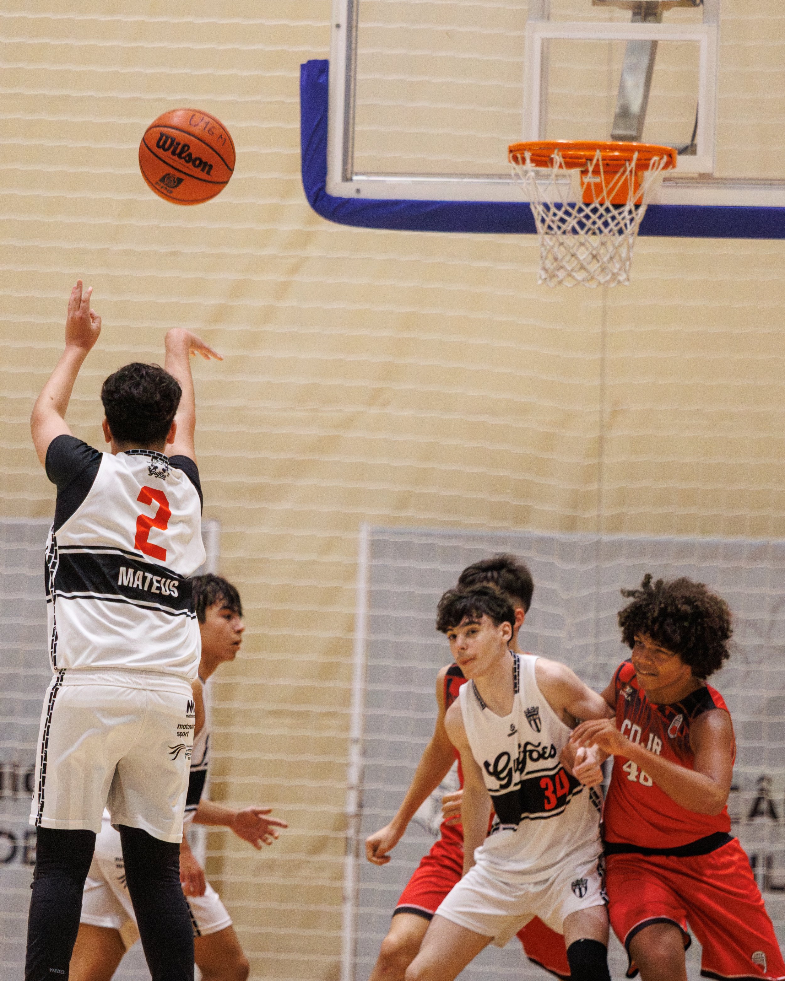 A basketball game with players trying to rebound or block a shot near the basket, with a basketball in mid-air heading towards the hoop.