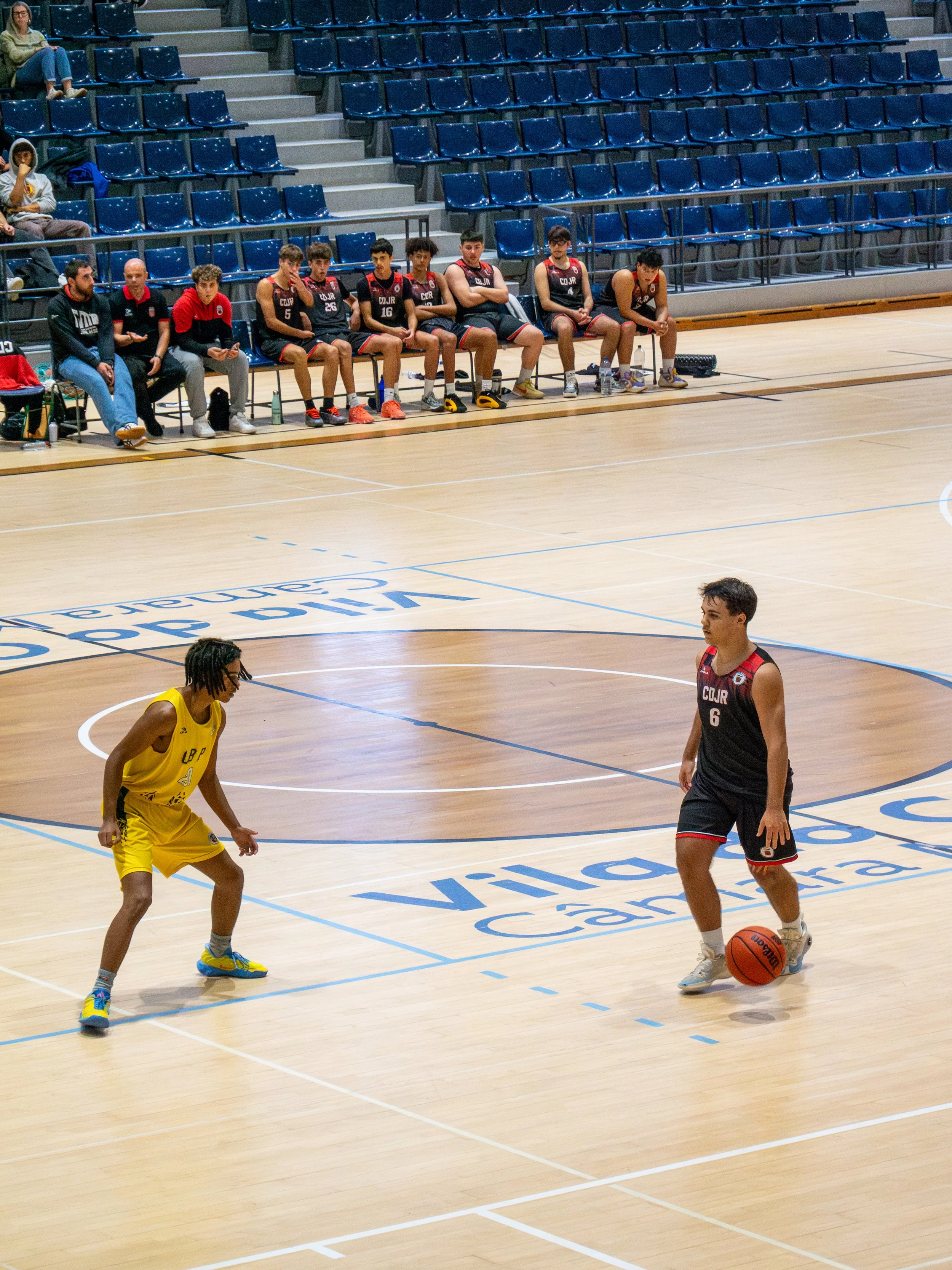 A basketball game in progress with two players on the court and a team sitting on the bench in the background.
