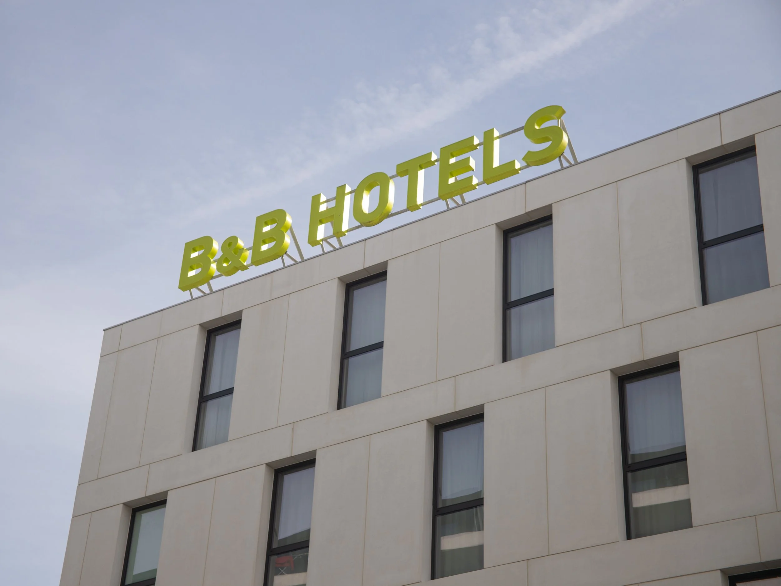 Exterior of a hotel building with a sign on the roof that reads 'B&B HOTELS' in large, yellow-green letters.