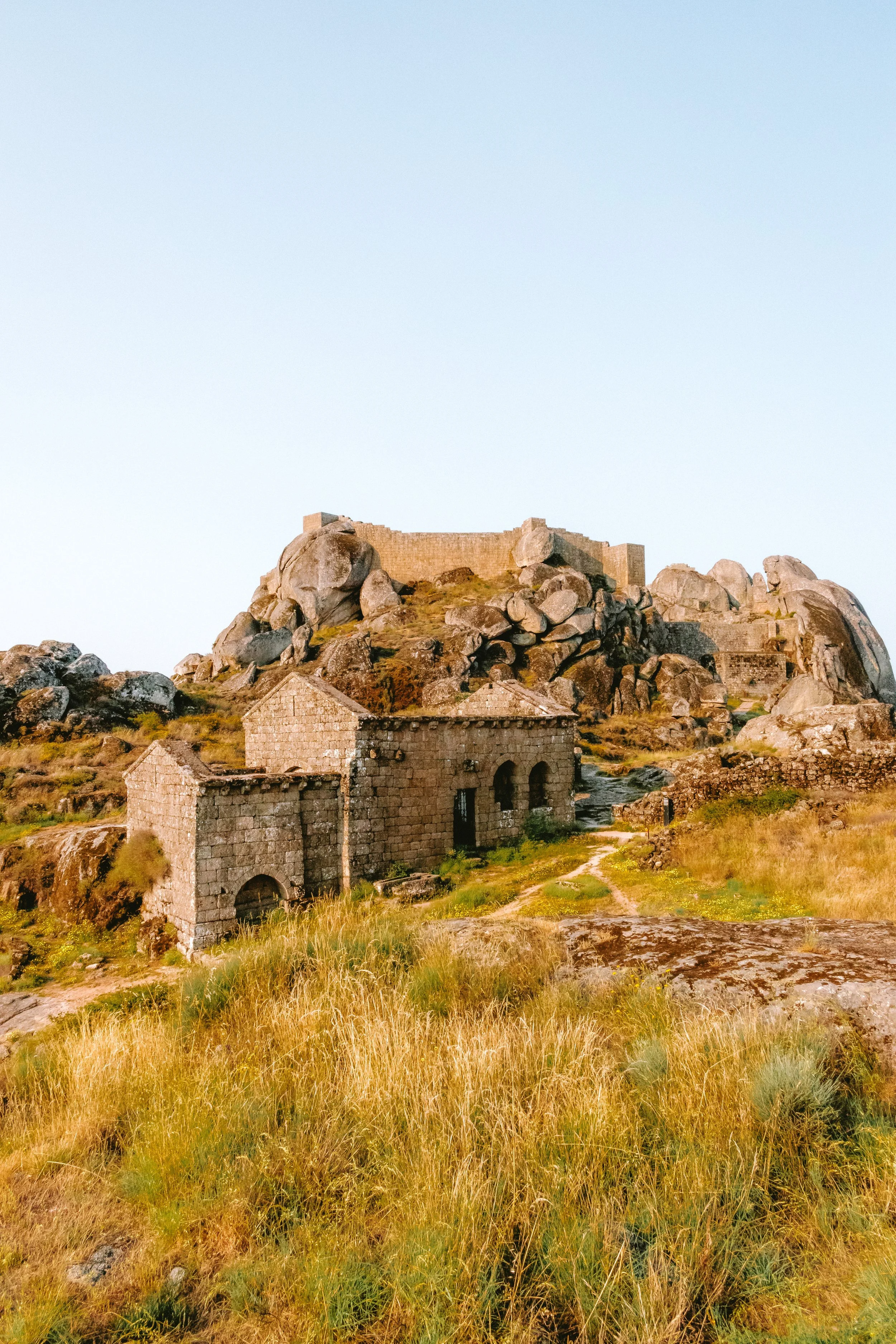 Stone buildings and ruins on a rocky hill with a clear blue sky.