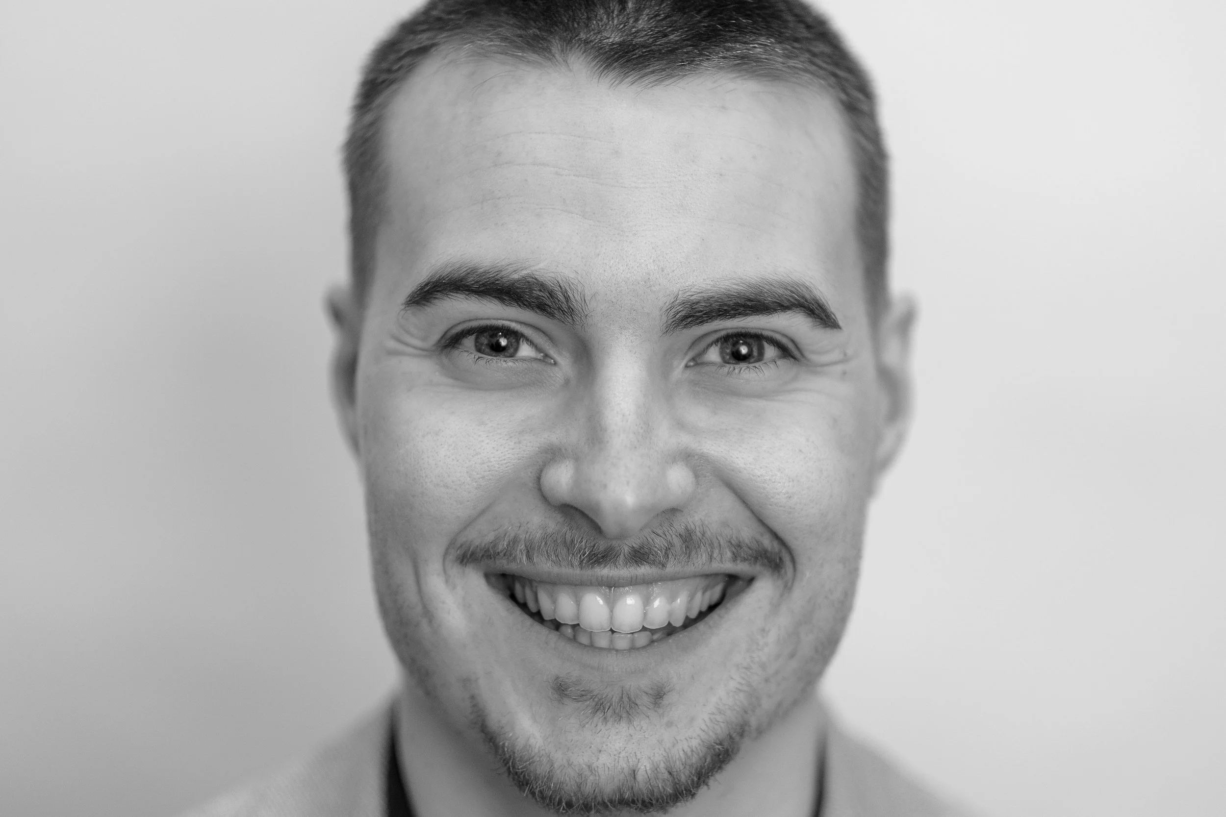 Black and white close-up photo of a smiling man with short hair, a mustache, and a goatee, looking directly at the camera.