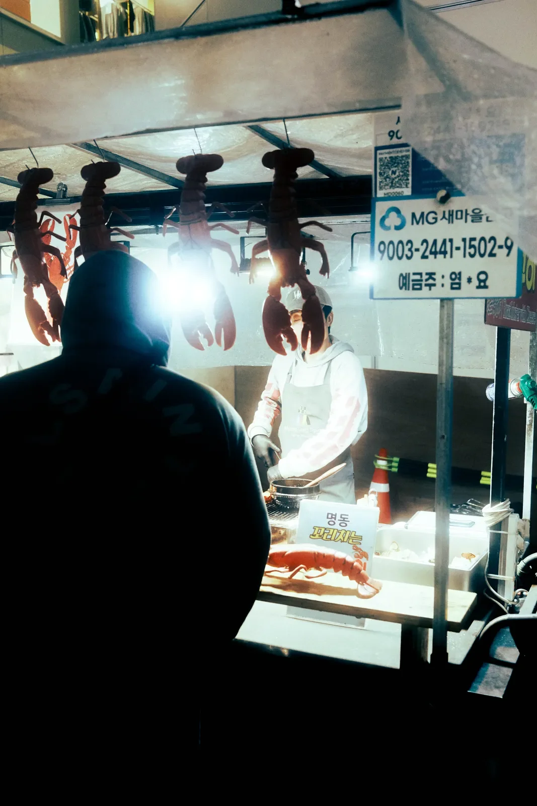 Vendedora preparando mariscos en un puesto de comida, con langosta sobre la mesa y cangrejos colgados en el techo del puesto.