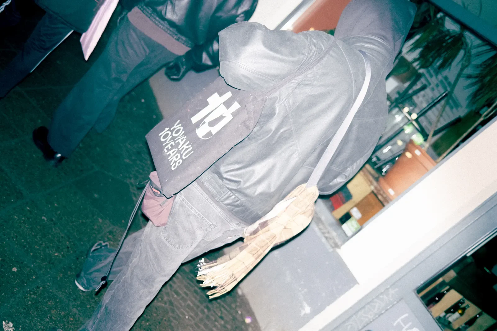 Persona con un saco gris y pantalones gris oscuro, con una bolsa negra que tiene el logo de UNICEF y la palabra 'YOUTH' en la espalda, en un espacio interior con plantas y estanterías con objetos.