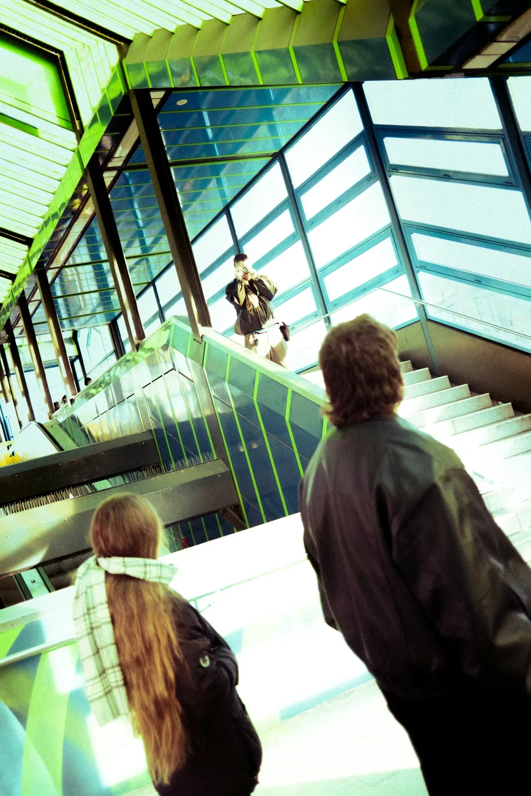Tres personas observando a otra persona en una escena moderna de interior con paredes de vidrio y estructura verde.