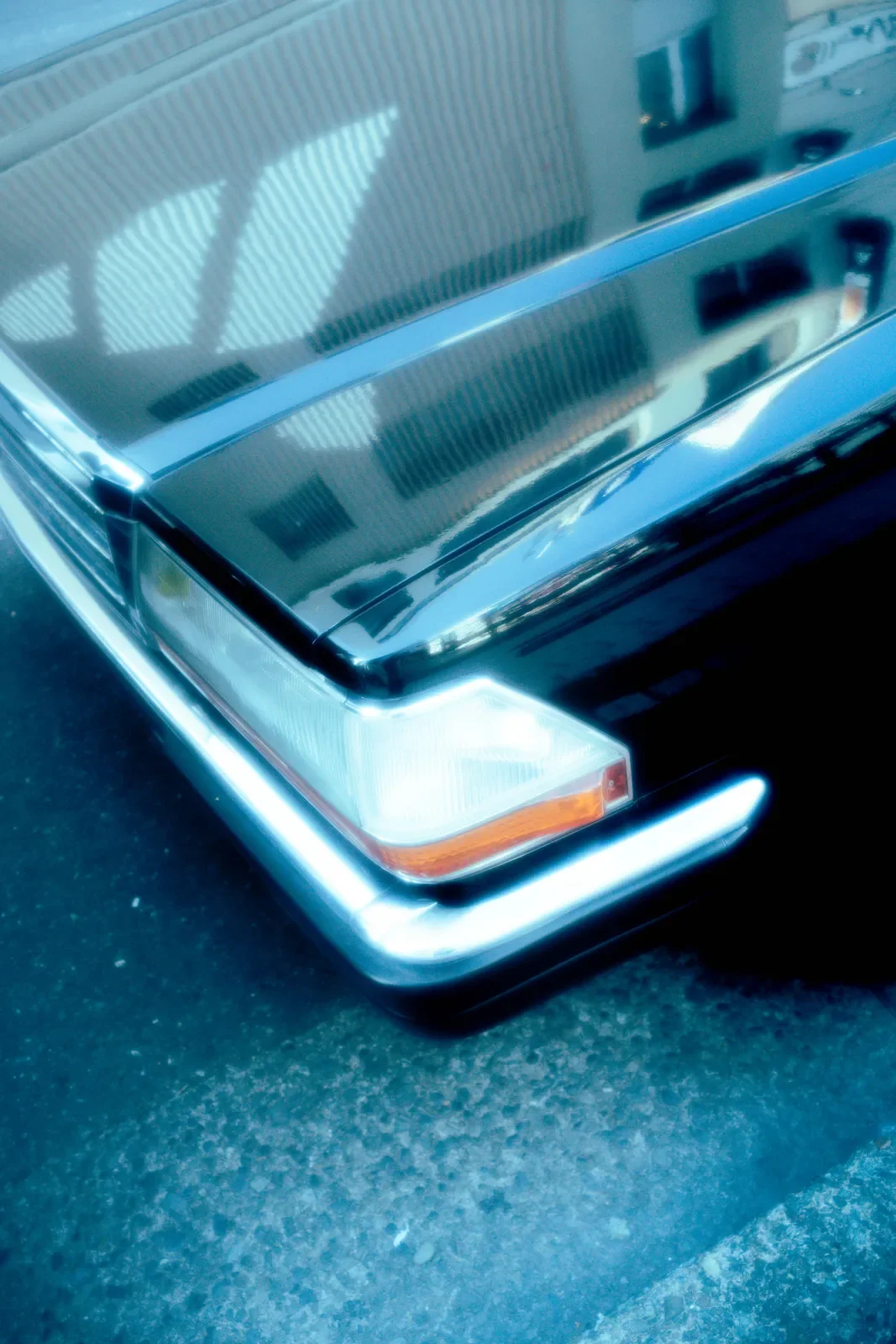 Primer plano del parachoques y faro delantero de un coche negro clásico con reflejo de edificios en el capó.