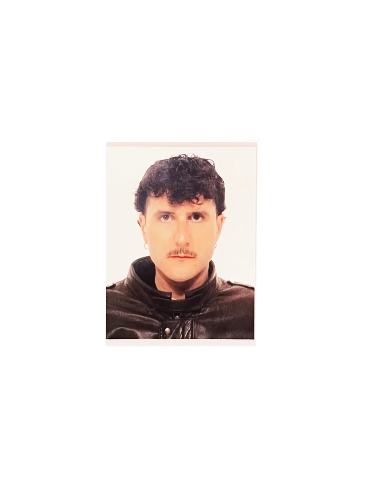 Retrato de un hombre con cabello oscuro, bigote y pendiente en la oreja, usando camiseta negra y chaqueta de cuero, en fondo blanco.