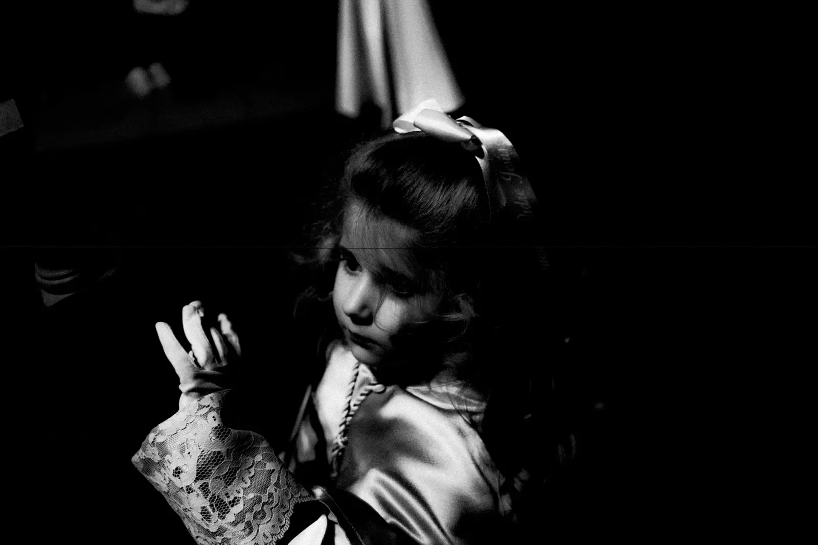 Retrato en blanco y negro de una joven con un lazo en el cabello, vestida con una blusa de encaje, en un fondo oscuro.