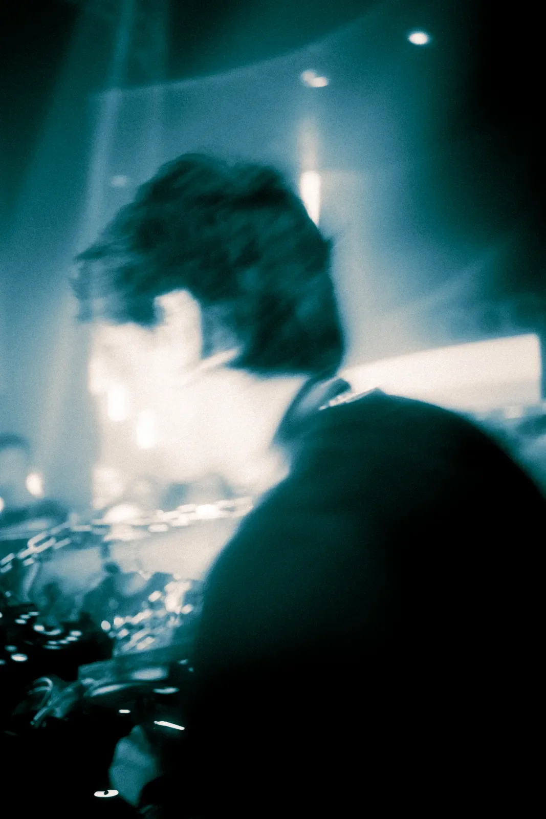 Persona con cabello oscuro y largo, de espaldas, en un entorno oscuro y luminoso