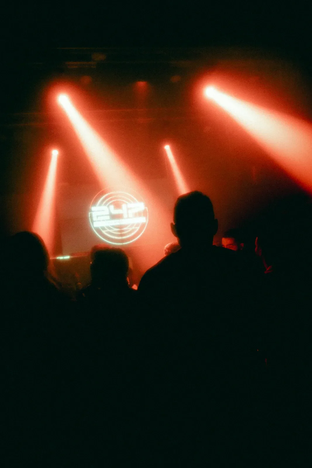 Persona frente a una pantalla con un logotipo circular y el número 24, en medio de luces rojas de escenario