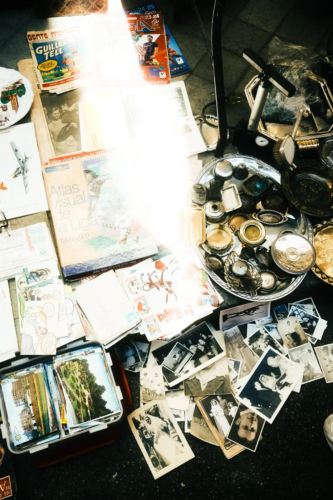 Colección de mapas, fotografías antiguas y objetos varios en una mesa, con un scooter en el fondo. Fotos en blanco y negro y en color, artículos de papelería y memorabilia vintage.