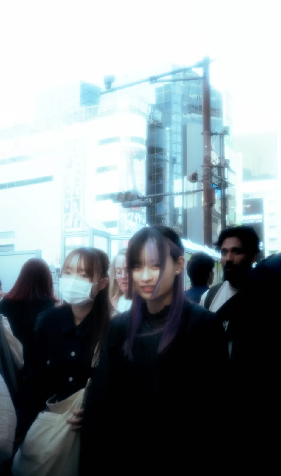 Personas en una calle concurrida en un entorno urbano con edificios y señales luminosas.