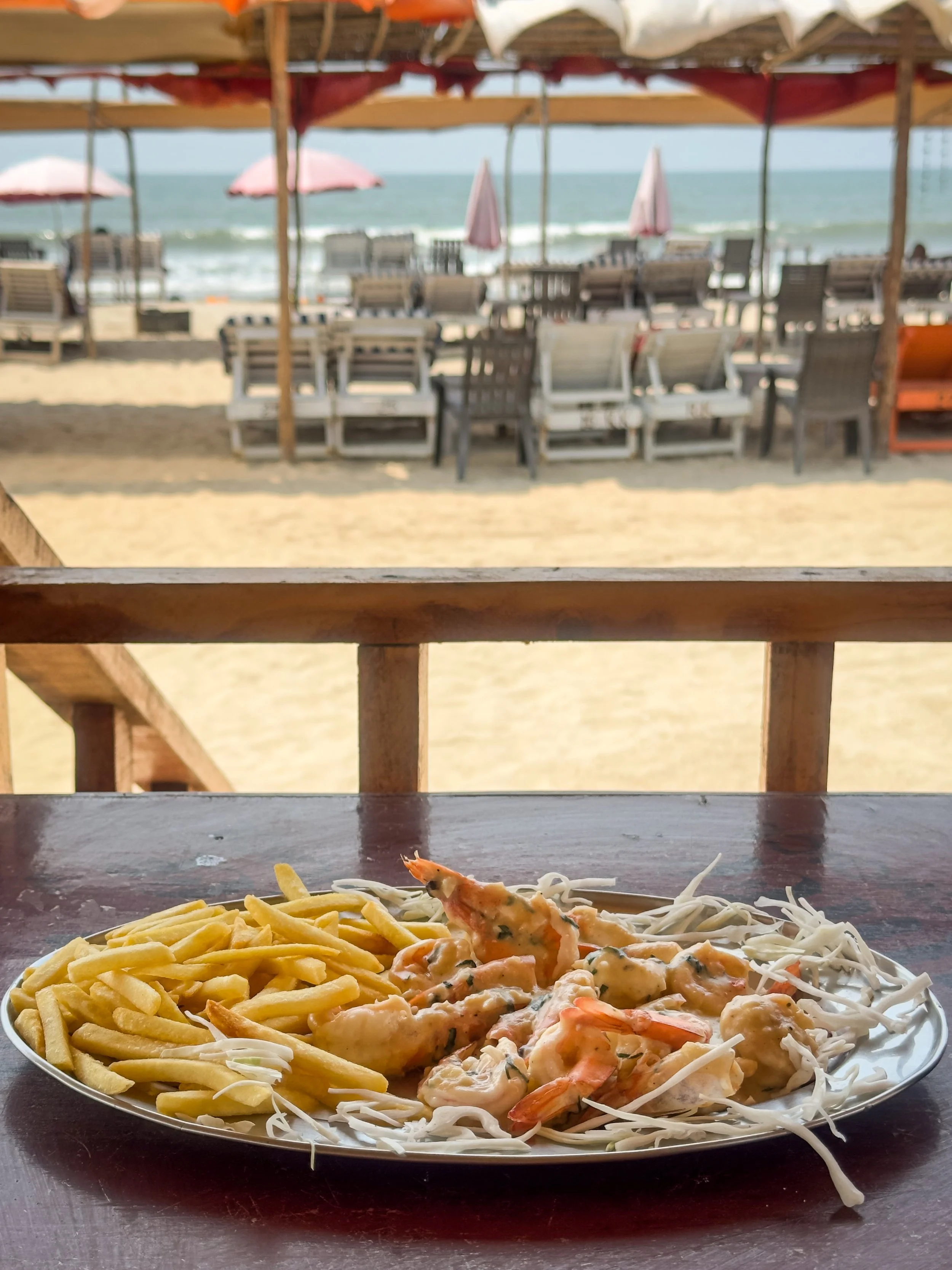 Seafood plate with fried shrimp and French fries on a table at the beach, with lounge chairs and umbrellas visible in the background.