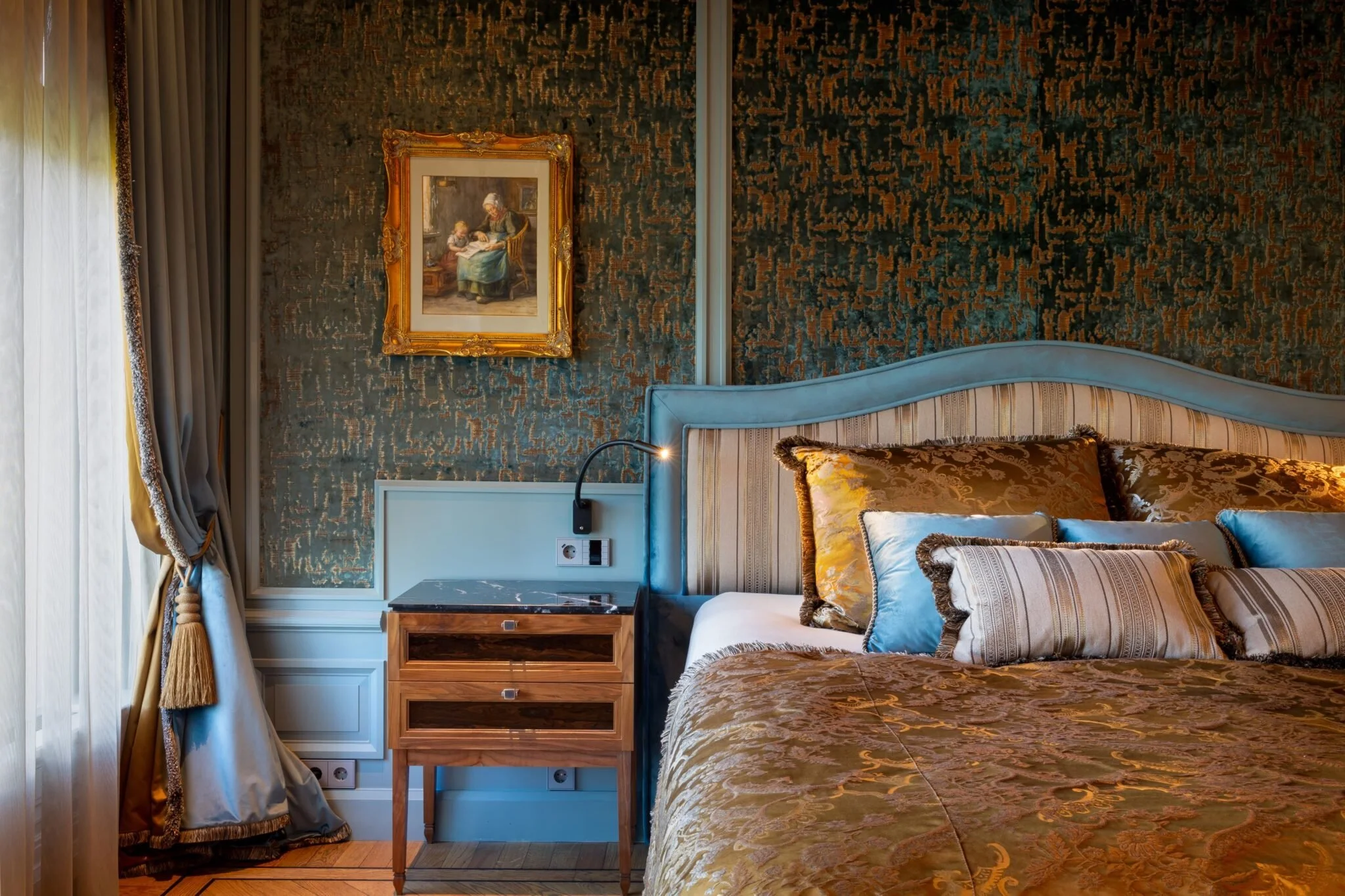 Een slaapkamer met een bed, sierkussens, een nachtkastje, een muurversiering, en een gordijn.