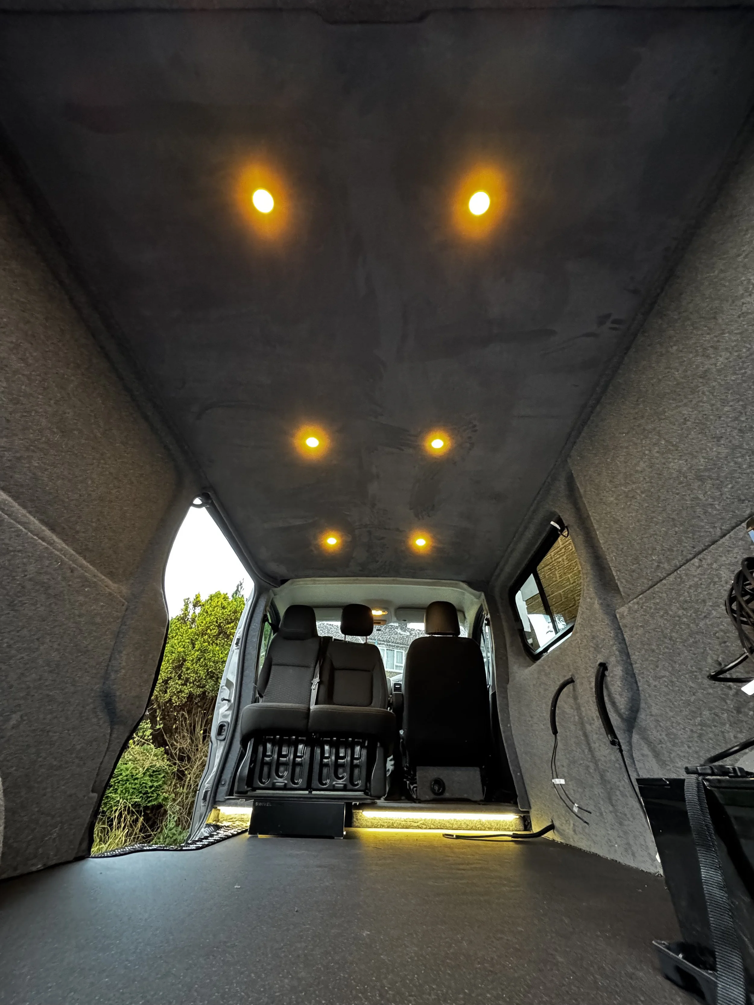 Interior of a partially converted van with gray upholstery and ceiling lights.