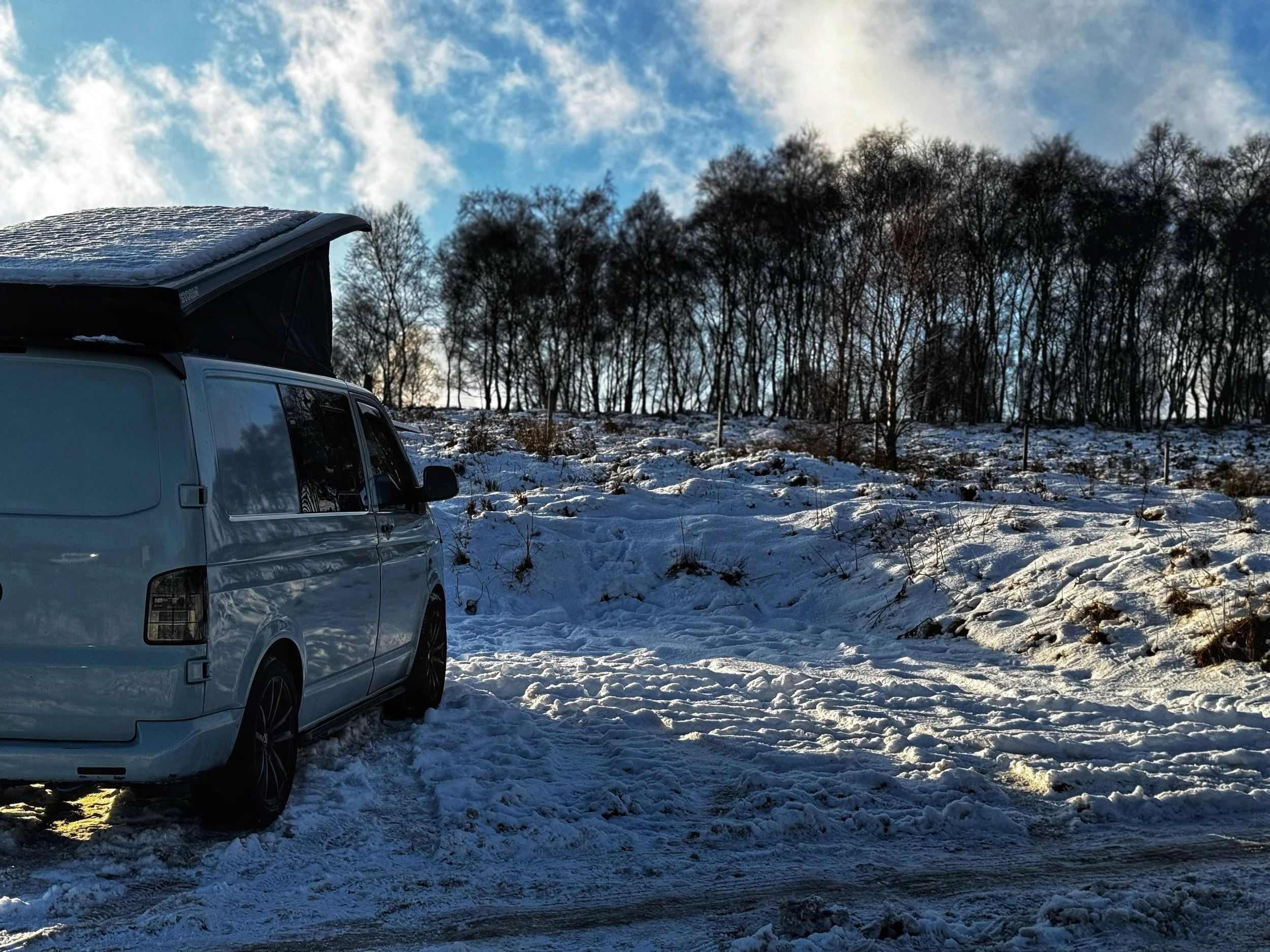 Camper van parked on snowy landscape with trees in the background.