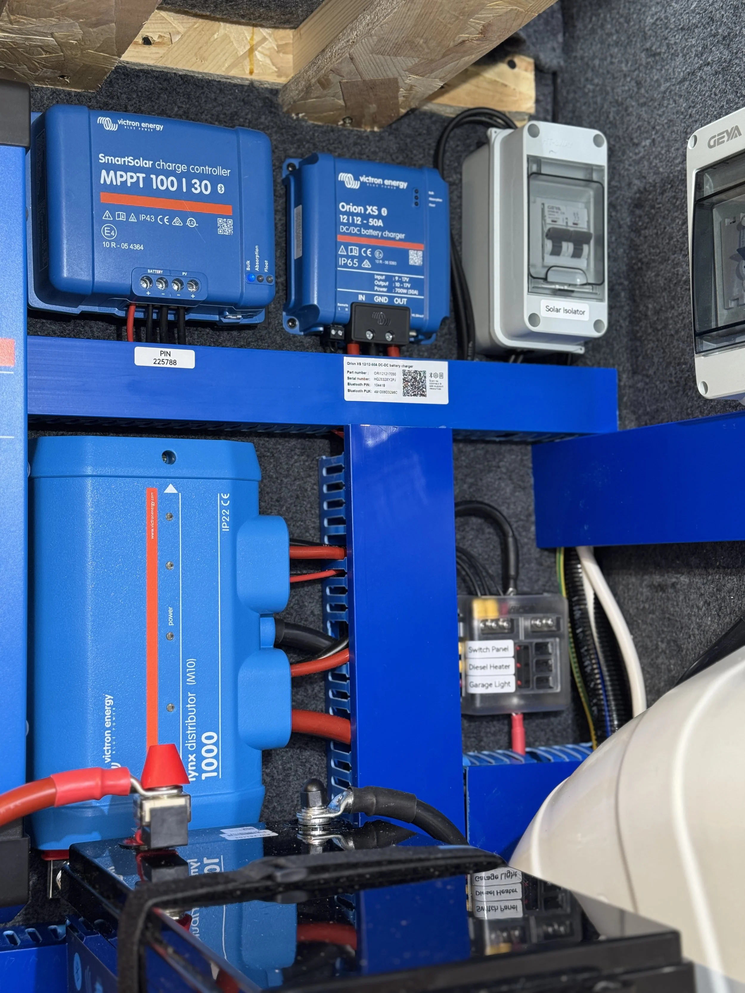 Electrical and solar power equipment including a blue micro inverter, a blue charge controller, a white circuit breaker, and a fuse box, all installed on a black surface with wiring.