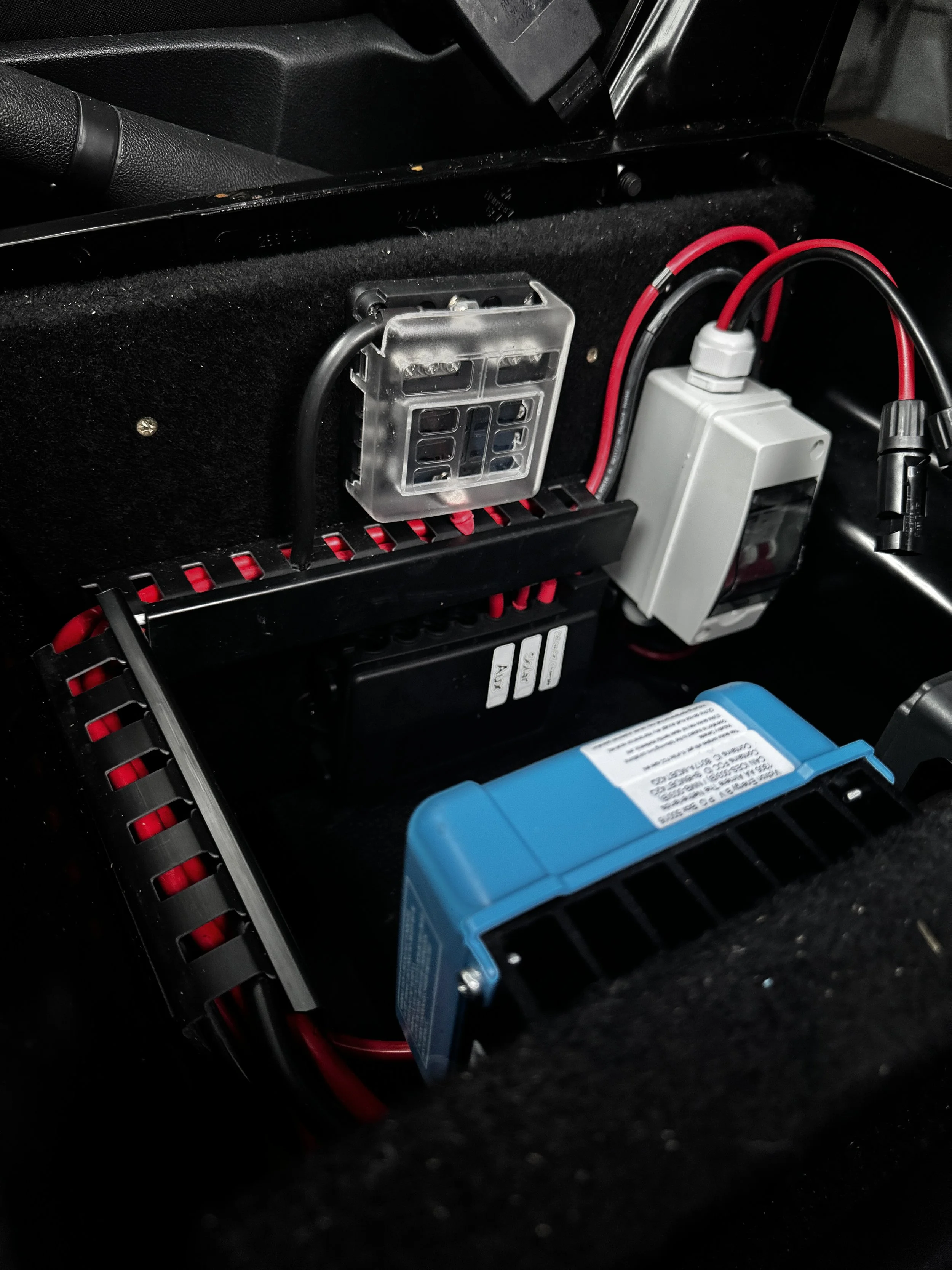 Inside a vehicle's compartment with electronic components, including a blue module, wiring, and a relay, mounted on a black panel.