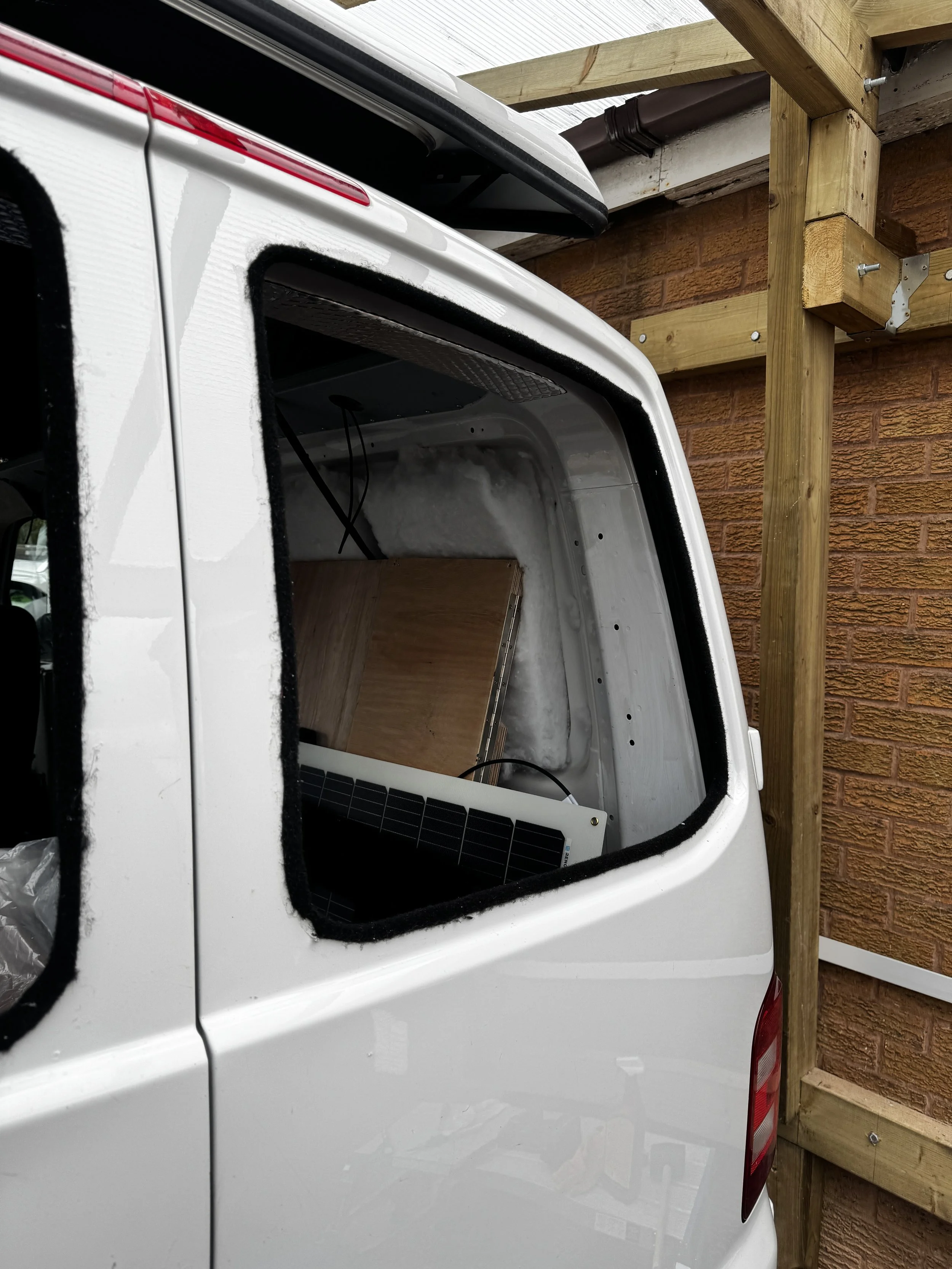 White van with a missing side window, interior visible, parked near a wooden structure.