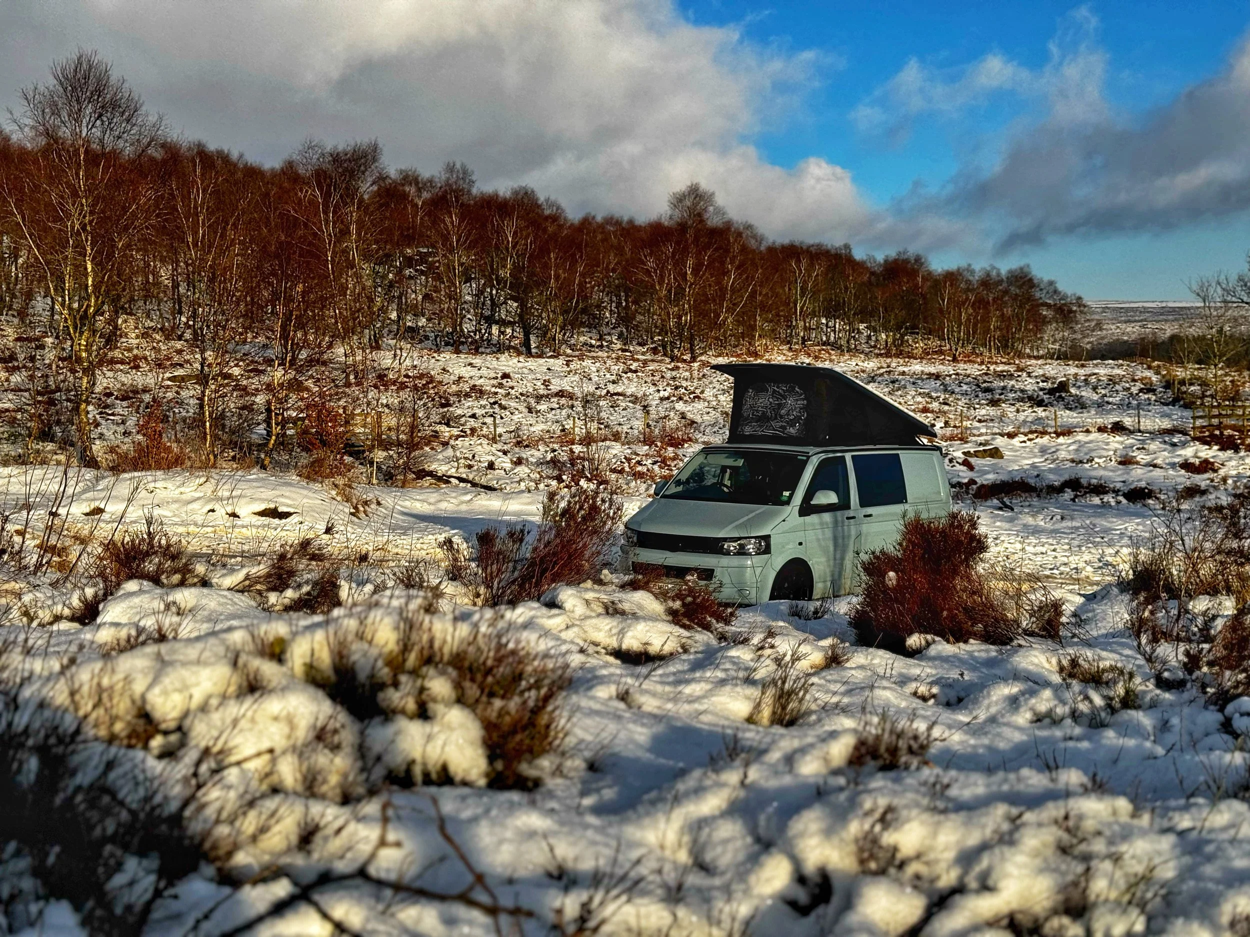 Camper van in snowy landscape with bare trees and blue sky