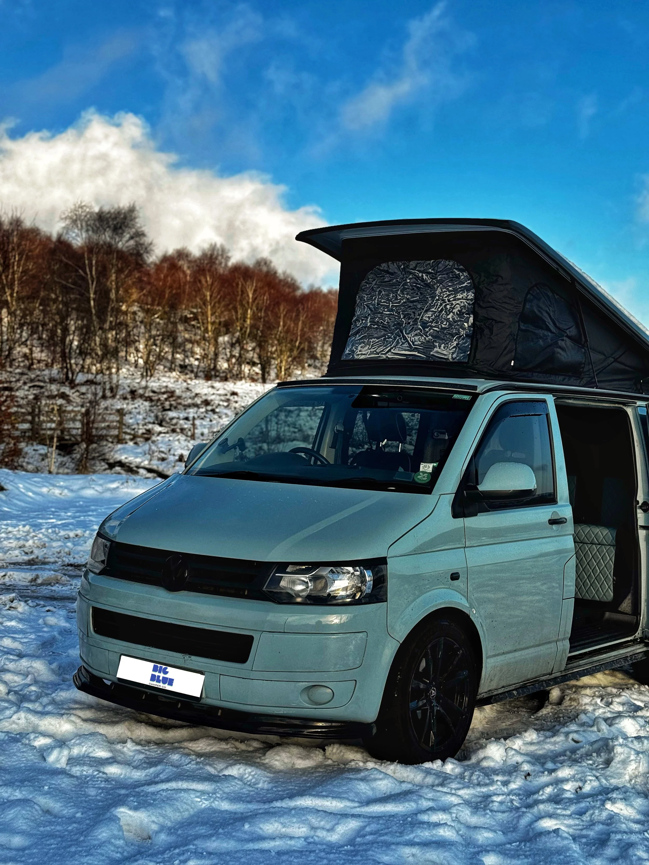 Camper van with pop-up roof parked on snow with trees in the background