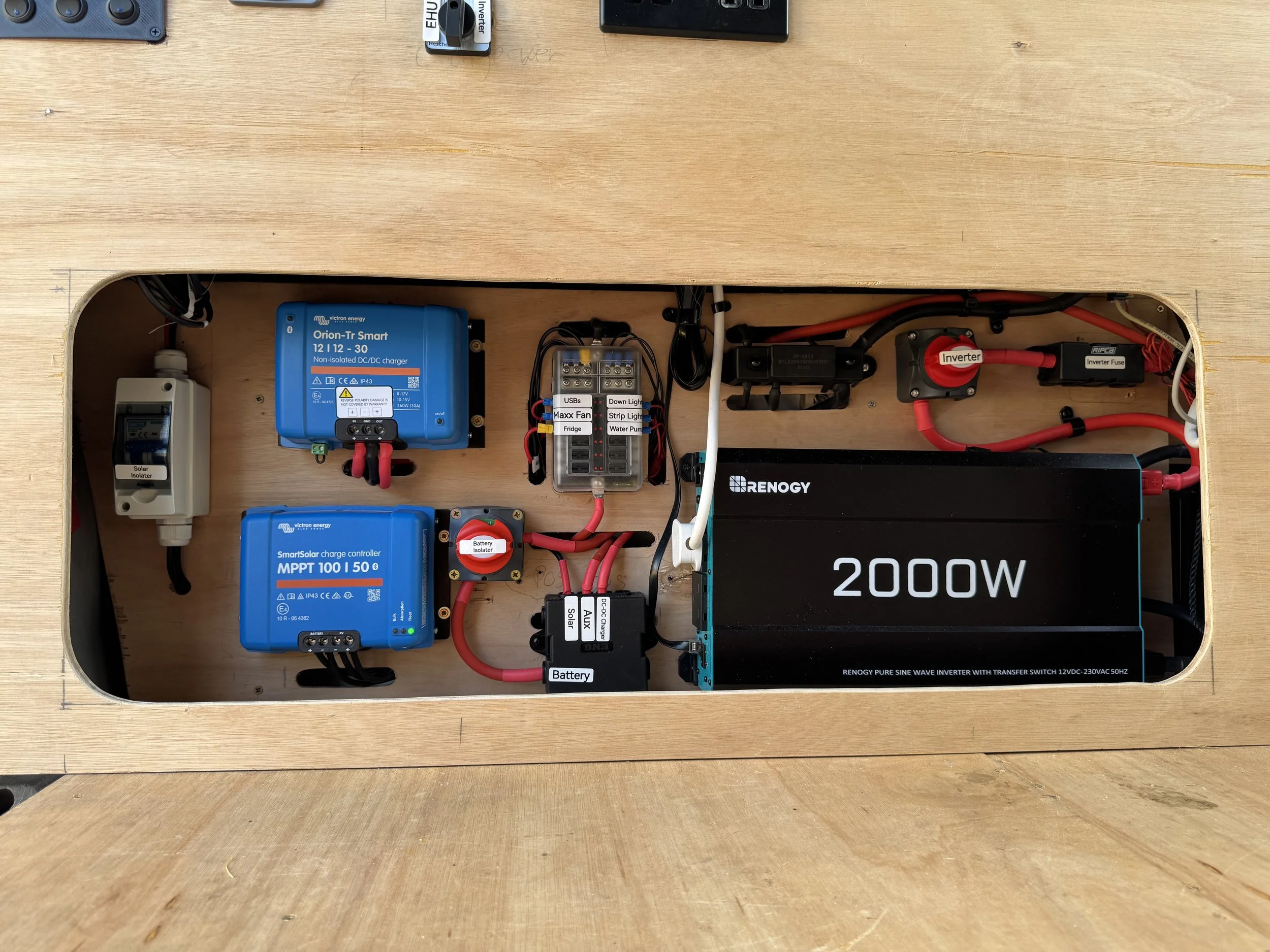 12v 230v Campervan electrical panel with Victron components, consumer units, wiring, fuse box, including a blue Orion-Tr Smart charger, a blue MPPT charge controller, a large black RENOGY inverter labeled 2000W, and other wiring and switches.