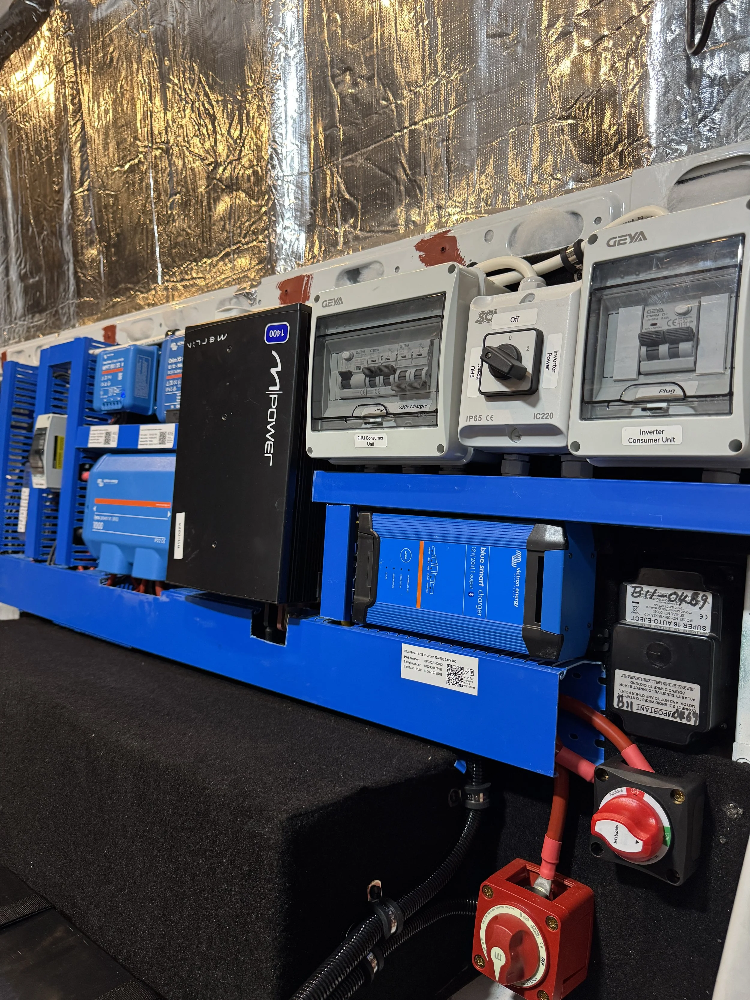 Electrical equipment including circuit breakers, transformers, and control units mounted on a blue rack, with wiring and safety switches, in an industrial or technical setting.