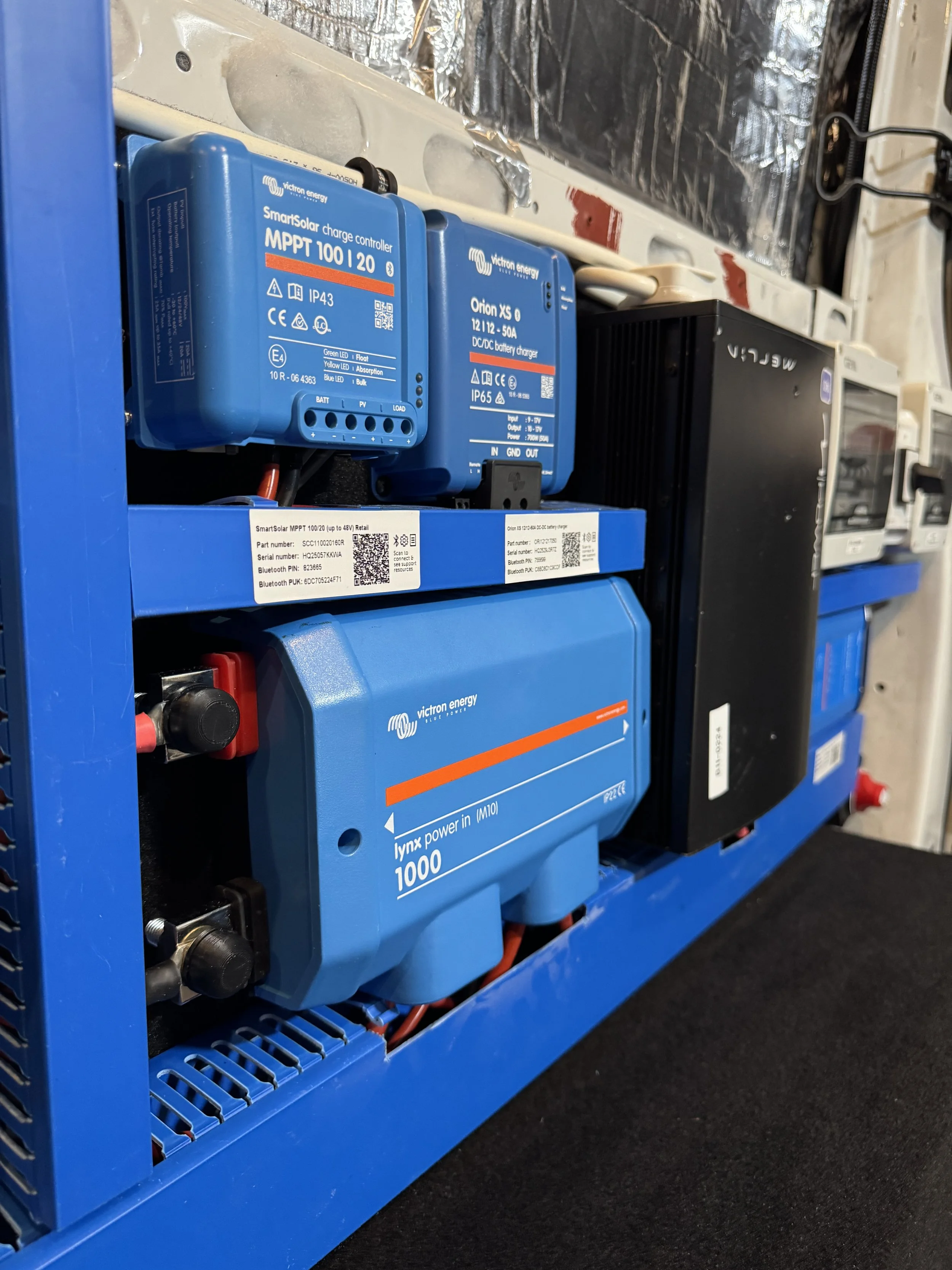 Arrangement of solar energy equipment, including a blue MPPT charge controller, a DC/DC battery charger, a power inverter, and wiring mounted on a blue metal rack.