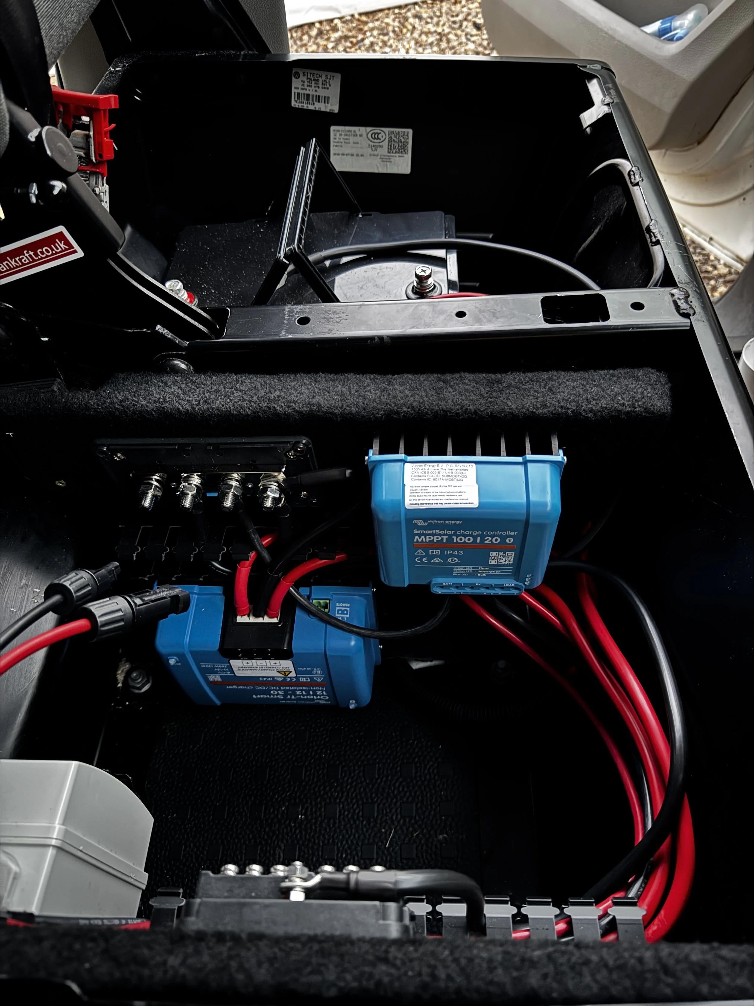 Electrical components with a blue MPPT charge controller and red and black wires inside a compartment.