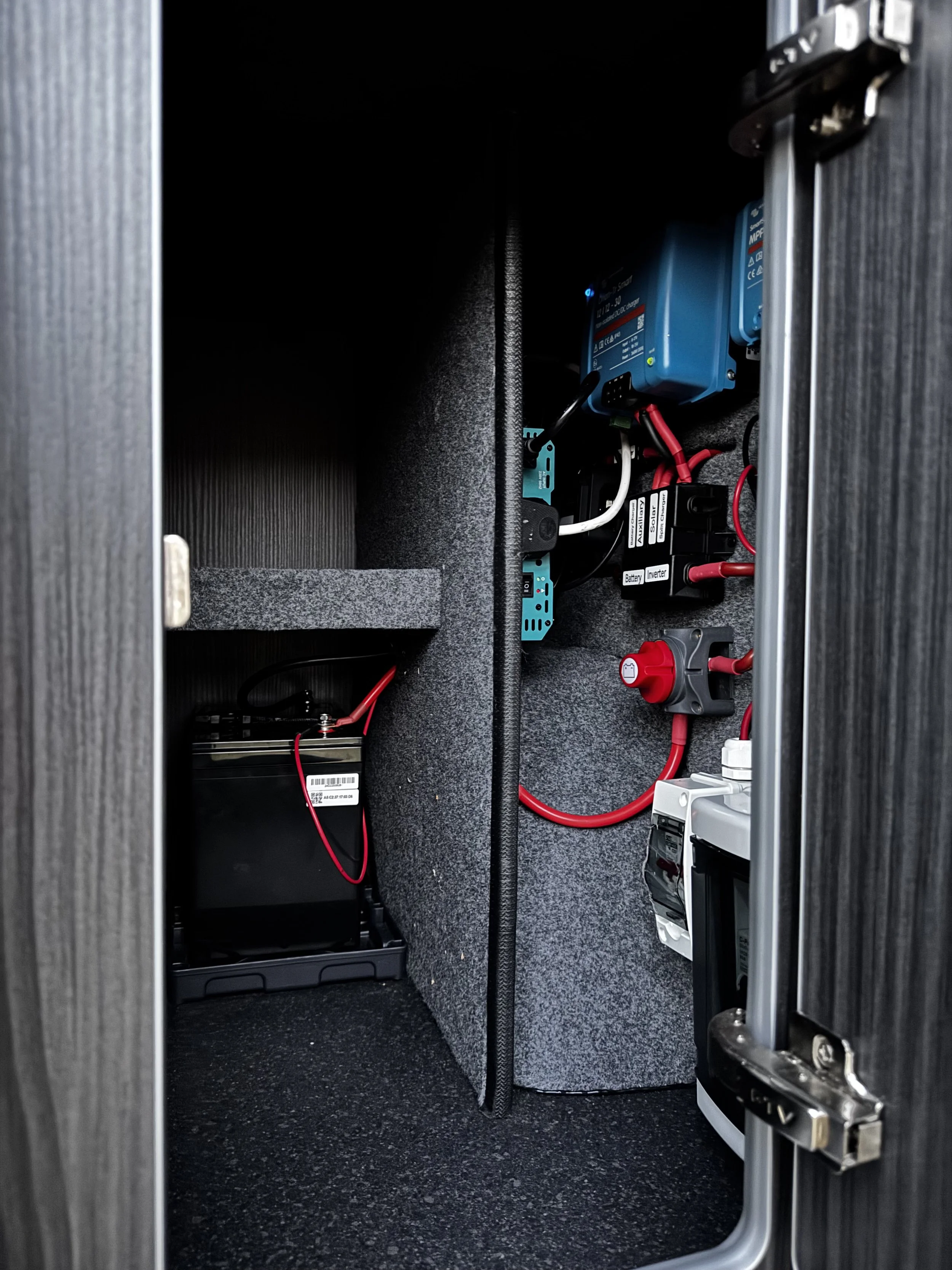 Interior view of an electrical cabinet with a battery and electrical components, including a blue charge controller and red wires.