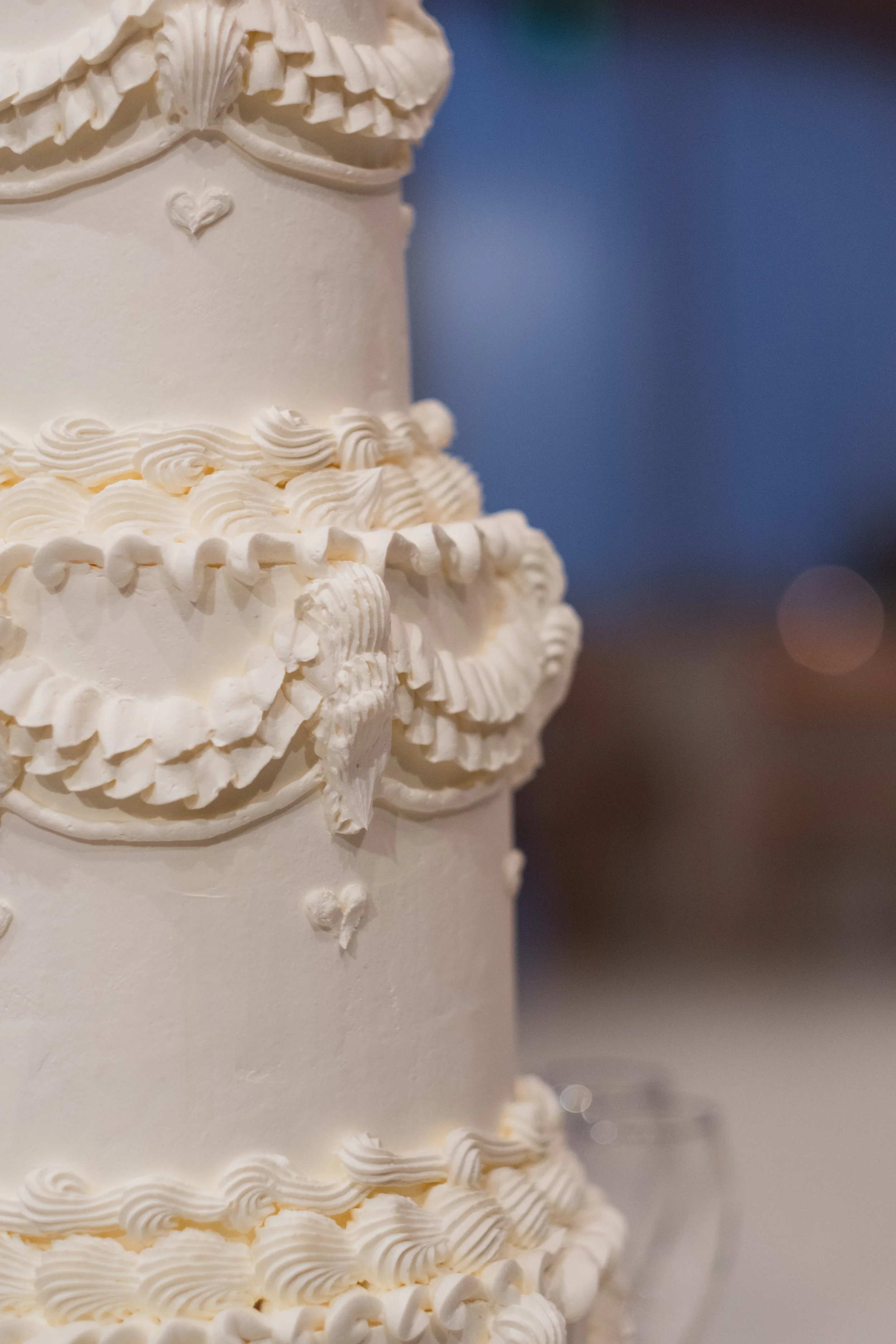 Close-up of a white, ornate wedding cake with decorative piping and sculpted details.
