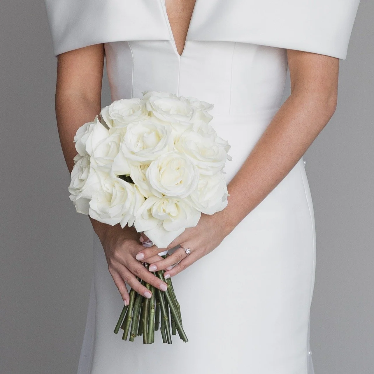 Bride in a white dress holding a bouquet of white roses.