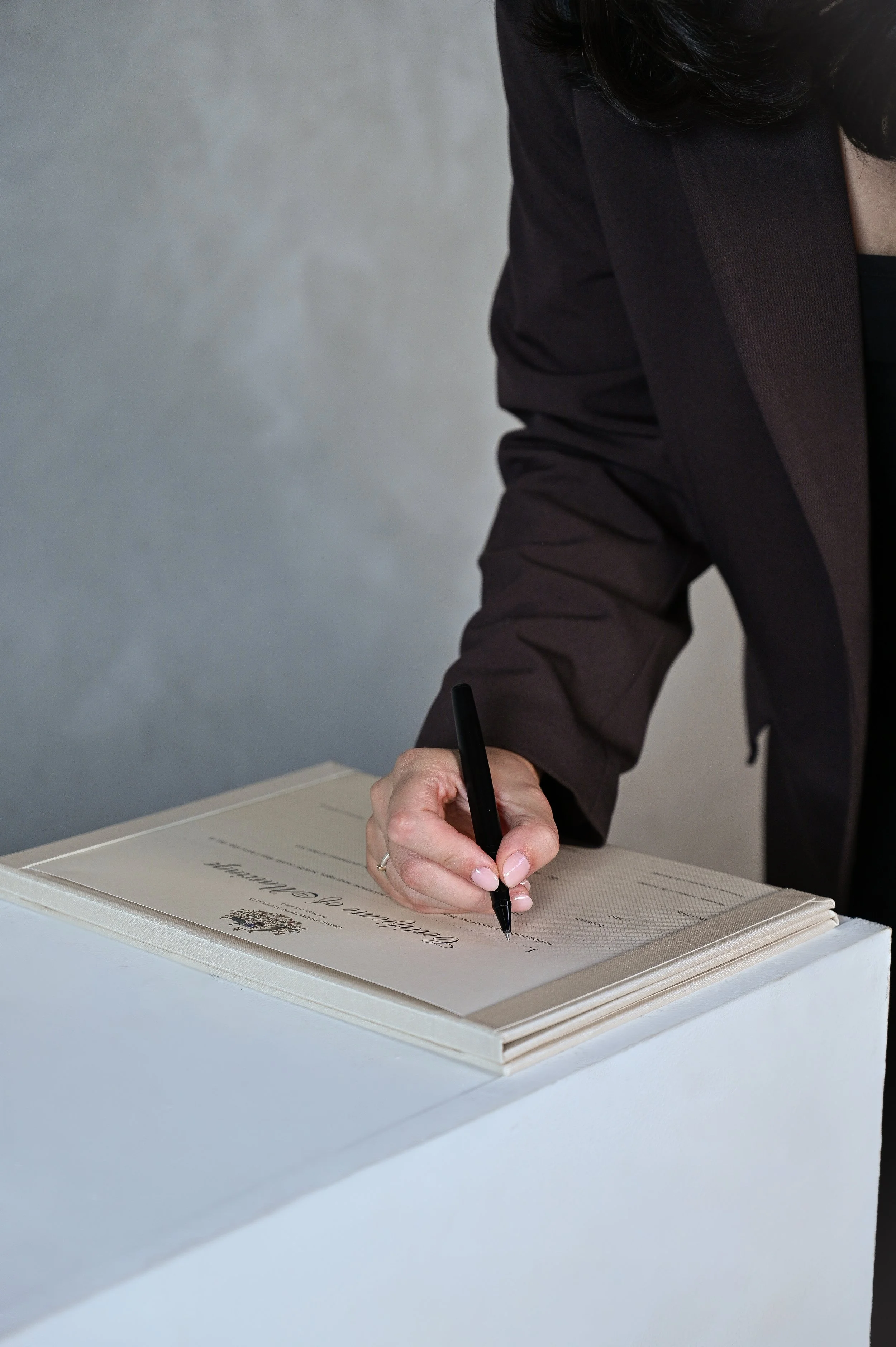 Person in a dark blazer signing a guestbook on a white surface