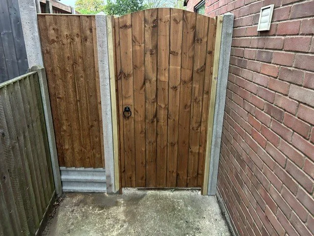 Wooden garden gate with metal latch, surrounded by brick and wooden fencing in an outdoor space.