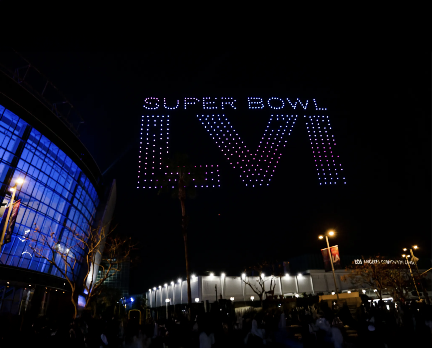 Nighttime view of a large illuminated sign that reads 'Super Bowl LVI' with a stadium in the background.