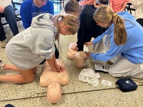 Two young women practicing CPR on a mannequin at a classroom training session.