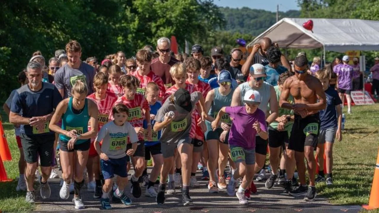 People start a race outdoors on a sunny day, with a mix of children and adults running together.