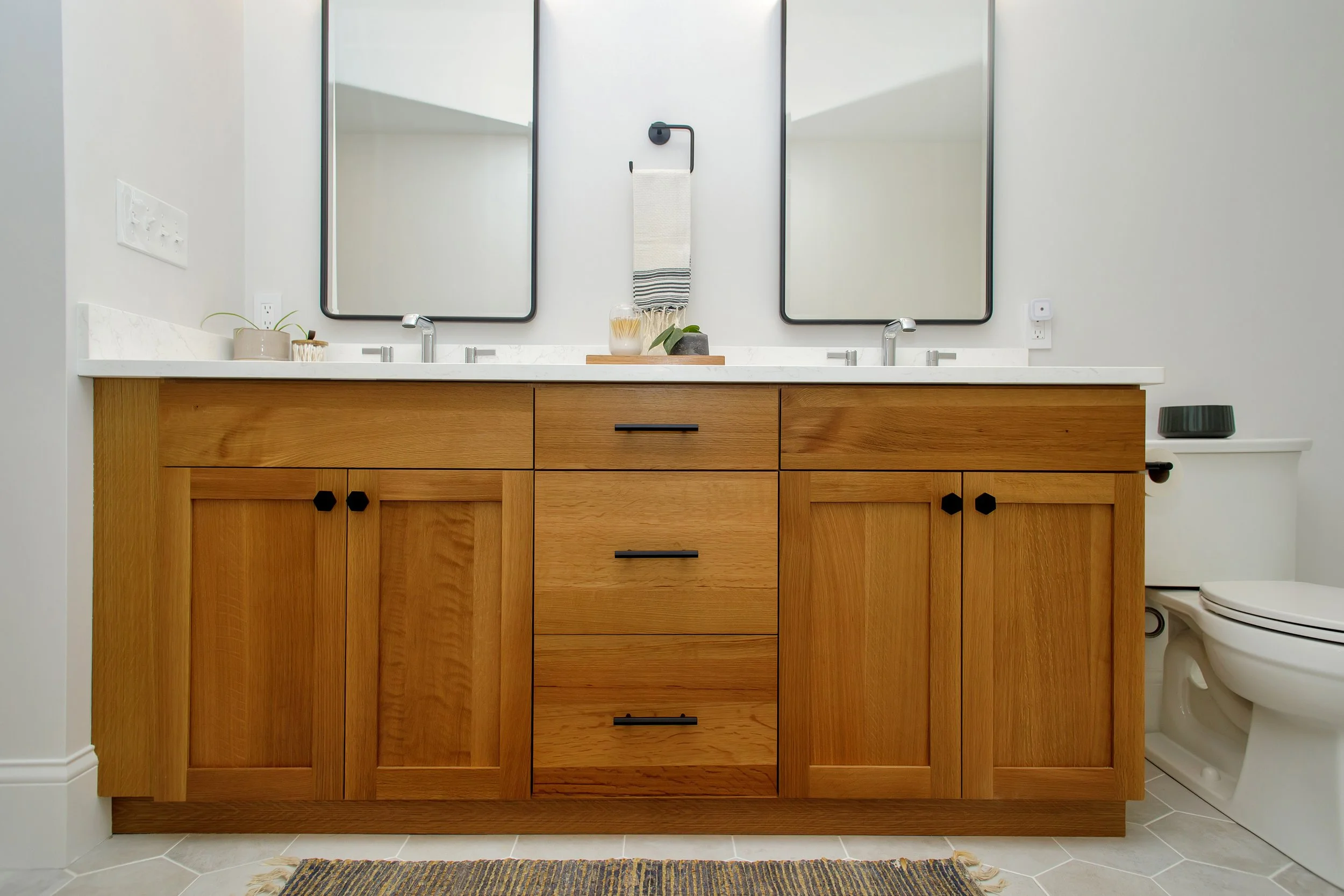 Modern bathroom with wooden vanity, two mirrors, twin sinks, and a toilet to the right.