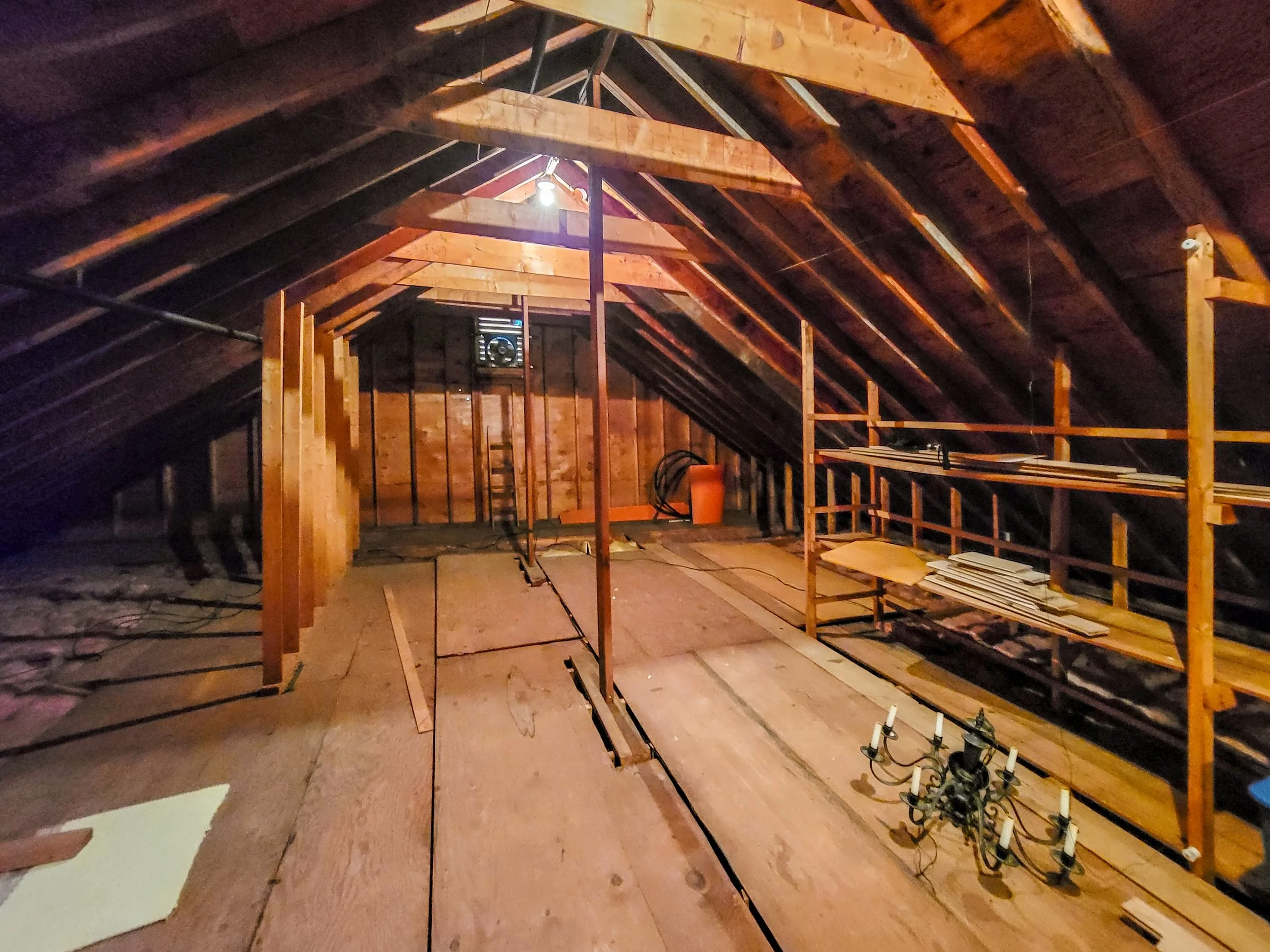 Attic space with exposed wooden beams, construction tools, and shelves with wooden boards.