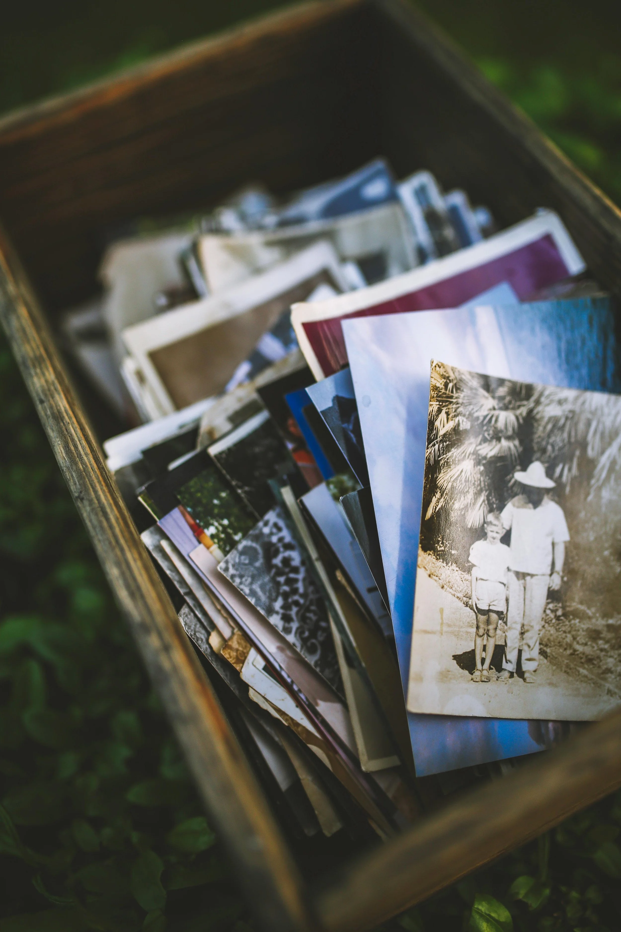 A wooden box filled with various printed photographs, some in color and some in black and white, featuring people and outdoor scenes.