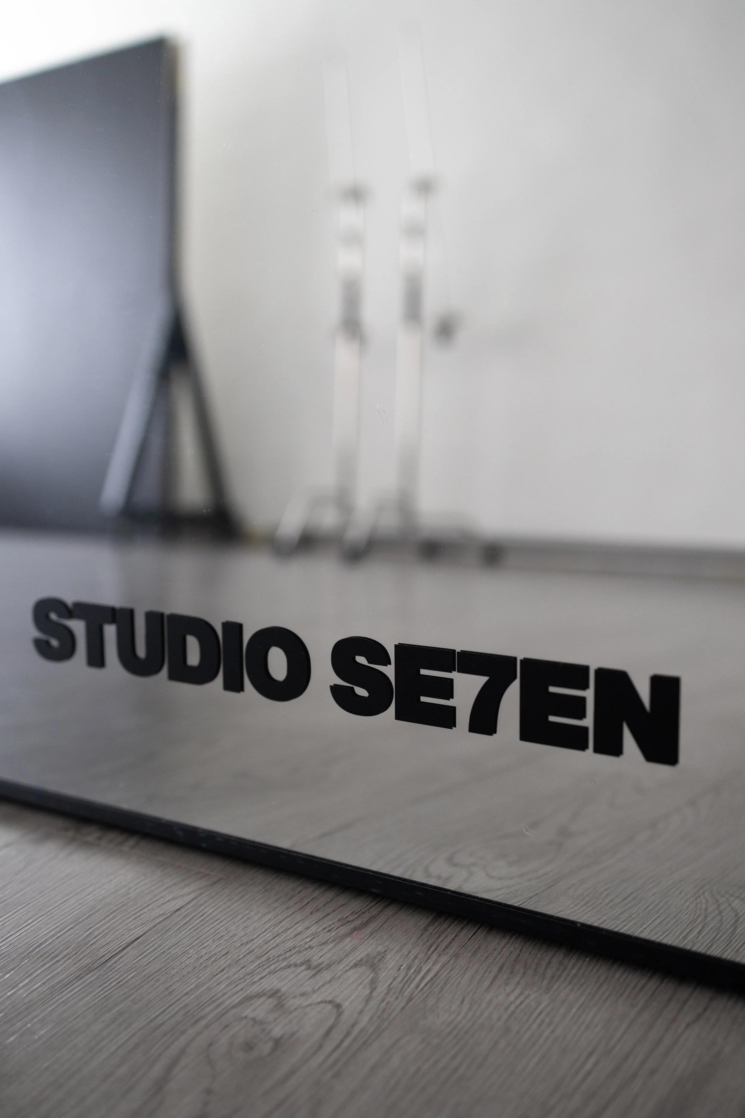 Close-up of a mirror with the words 'STUDIO SE7EN' written on it in black letters, reflected on a wooden floor.