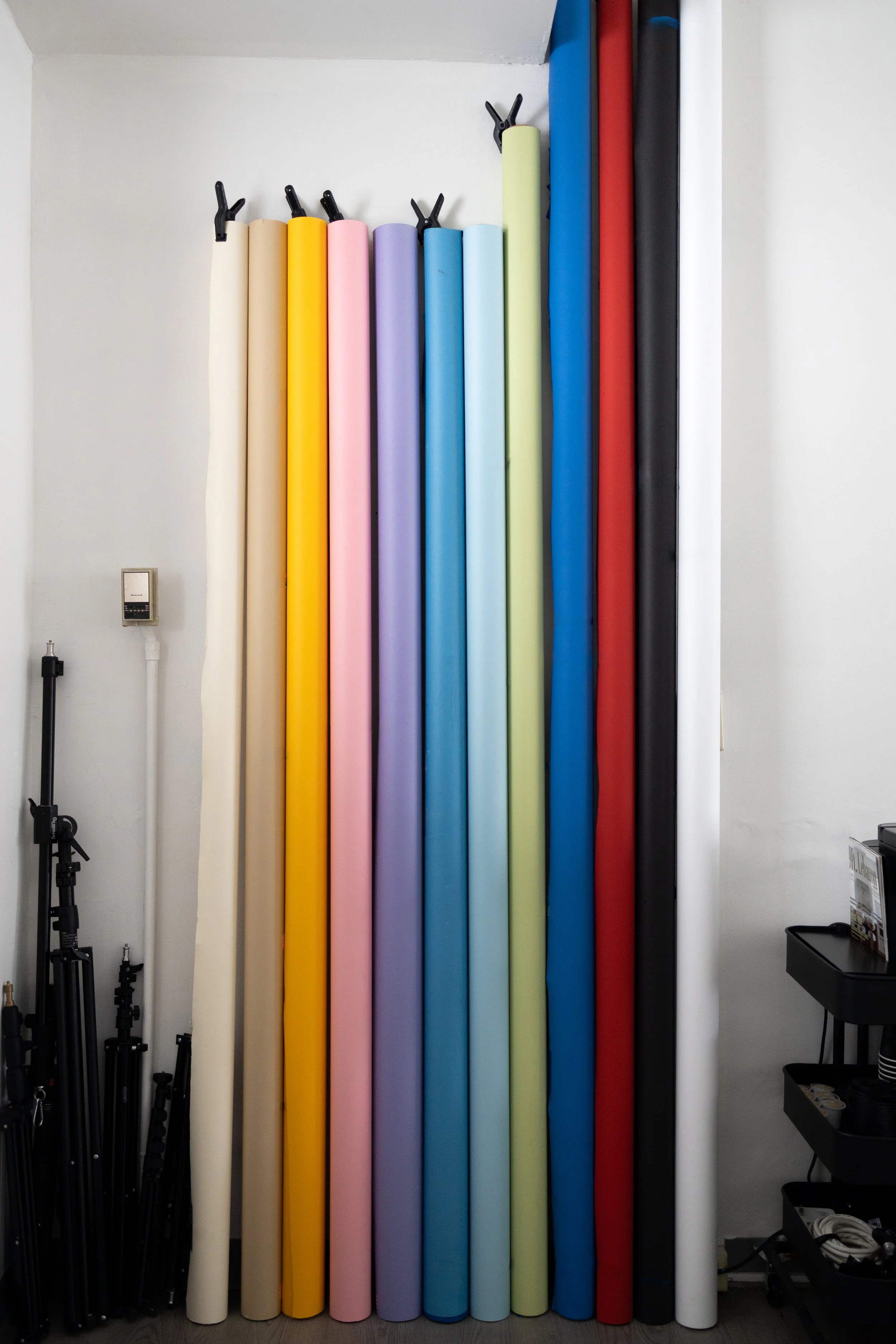 A collection of colorful photography backdrops in various pastel and bright colors, stored vertically on hooks in a studio setting.